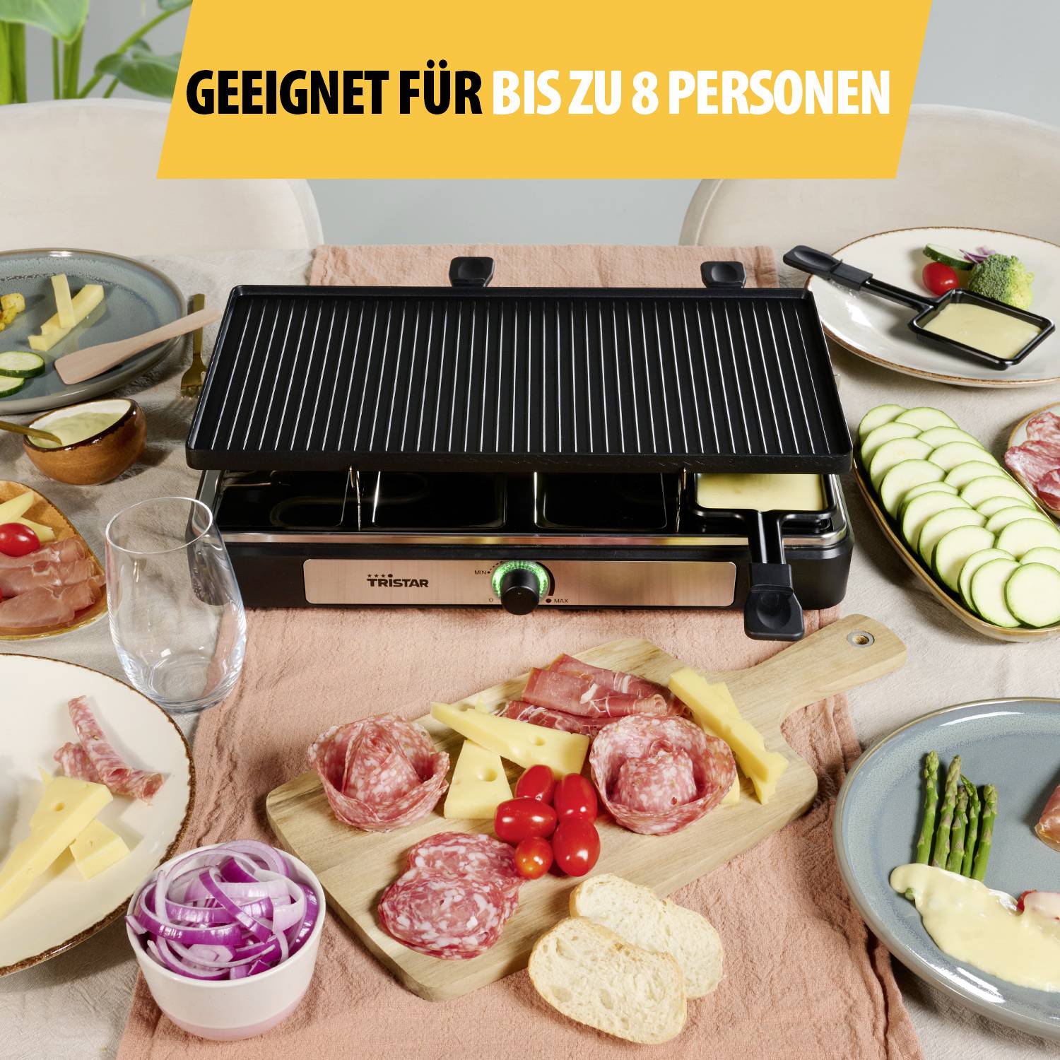 En bordsgrill står i mitten av ett dukat bord med ingredienser för raclette: korv, grönsaker, ost, bröd. Text: 'Lämplig för upp till 8 personer'.