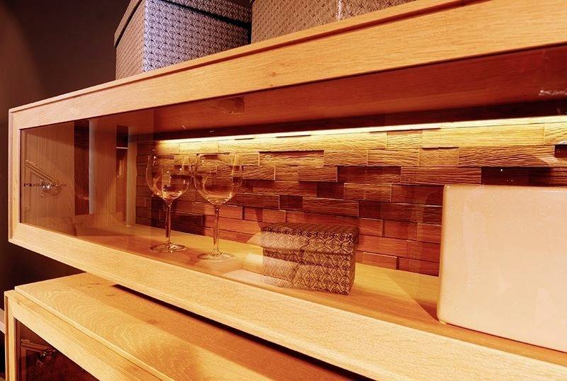 Trädhylla med glasfront, två vinglas och dekorativa lådor på upplyst träställning. Elegant design för heminredning.