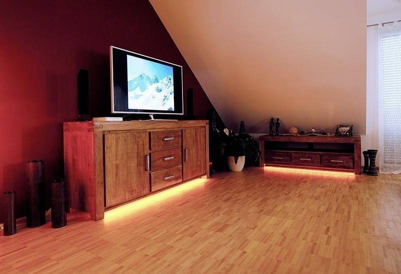 Ett vardagsrum med röda väggar, ett träskåp där en TV står, och LED-belysning på golv och skåp.