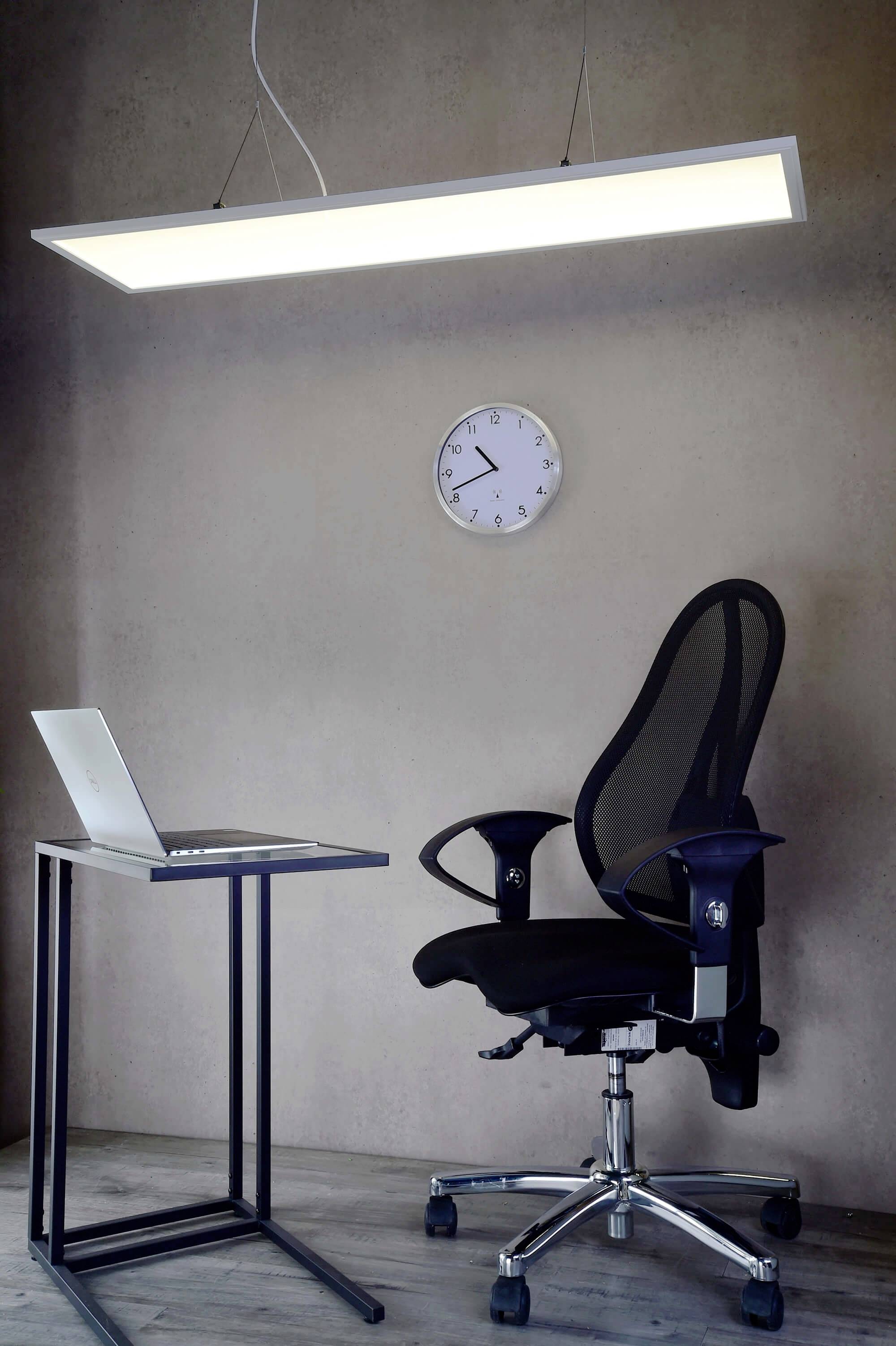 Ett modernt, minimalistiskt inrett rum med en bärbar dator på ett litet bord, en ergonomisk stol och en väggklocka.