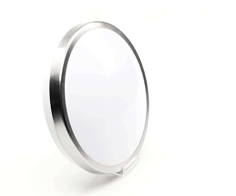 Rund LED-lampa med silverram mot vit bakgrund. Den står något lutad och vilar på ett litet stativ.