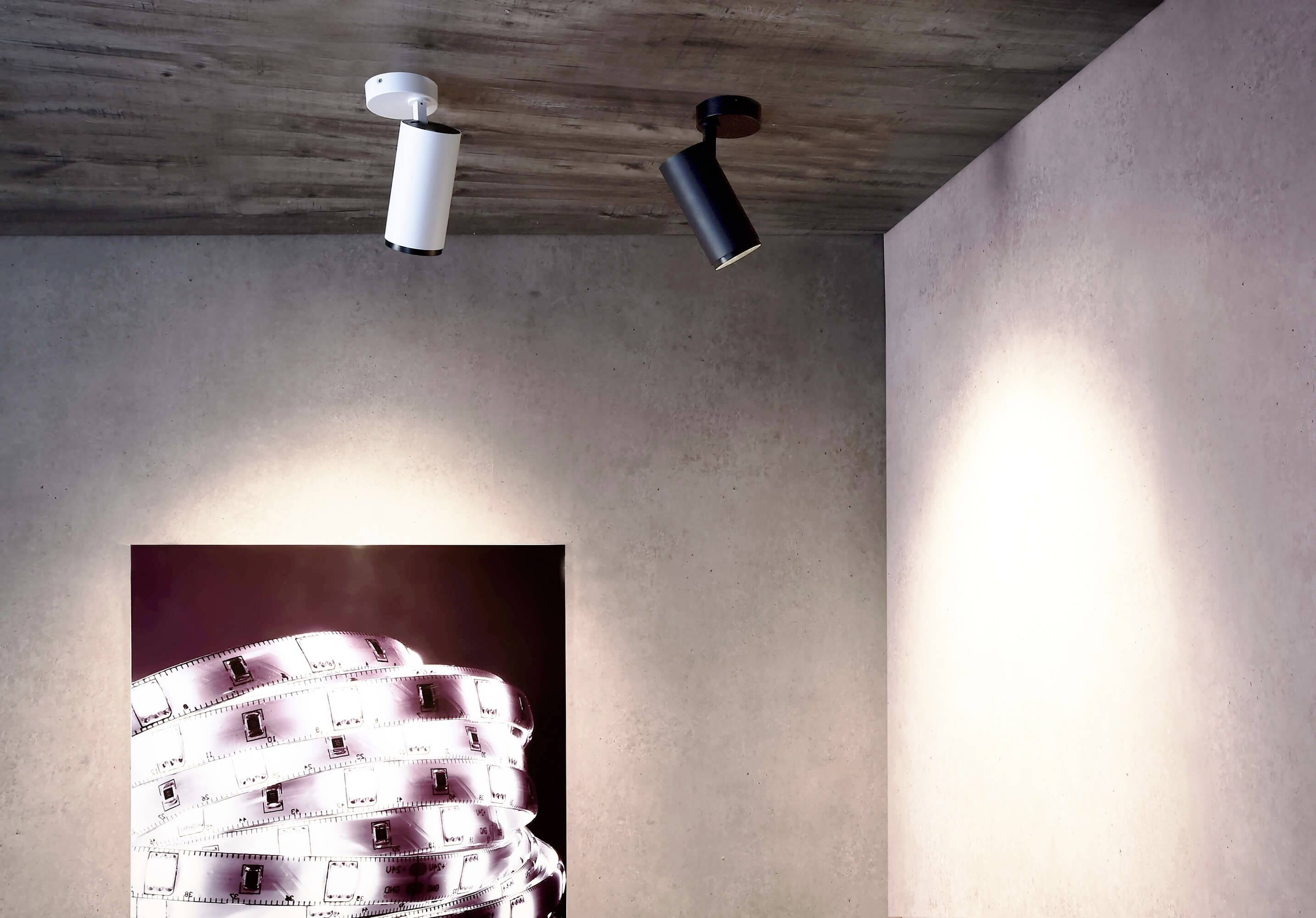 Ett rum med en konstprint av filmrullar på väggen. Två modernt utformade takspotlights belyser rummet från en betongpelare.