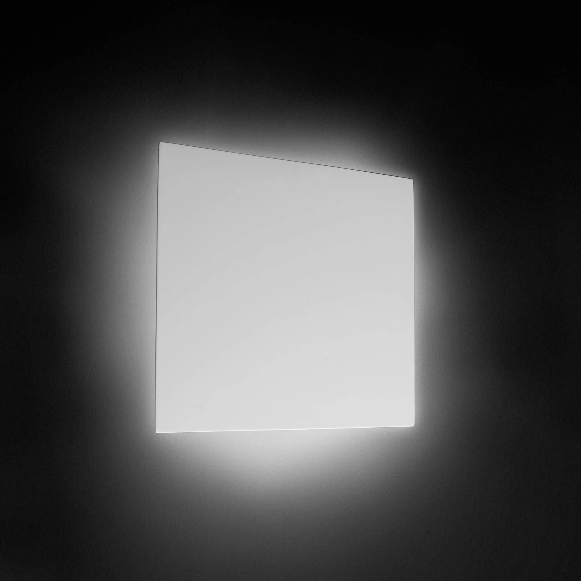 Lampa på en vägg med ett diffust, vitt sken. Minimalistisk design i en mörk omgivning.