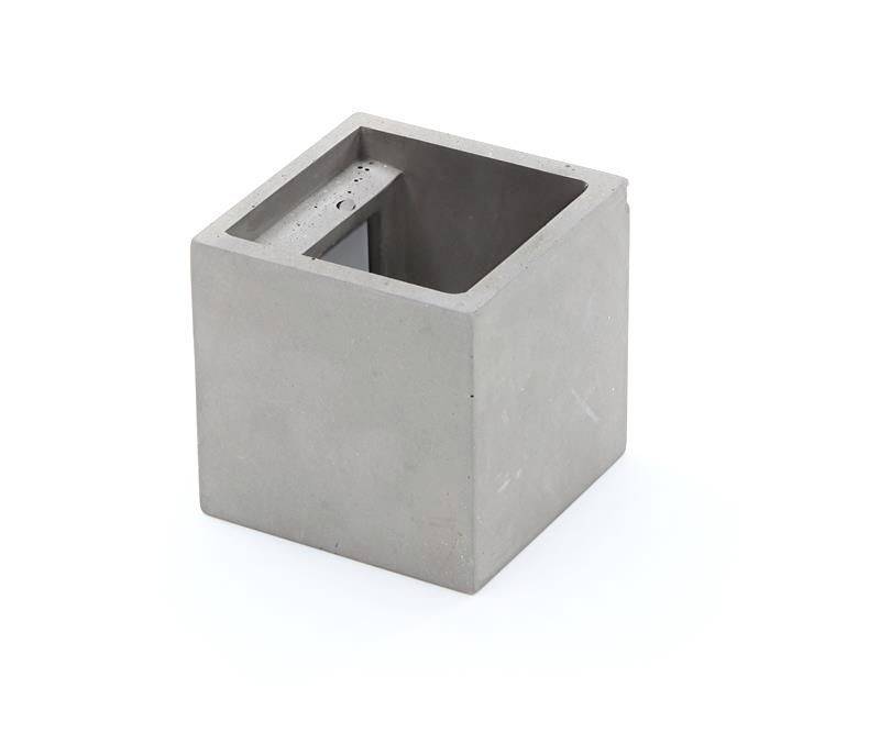 En kvadratisk, grå betongblock med ett hålrum i mitten, placerad på en vit yta.