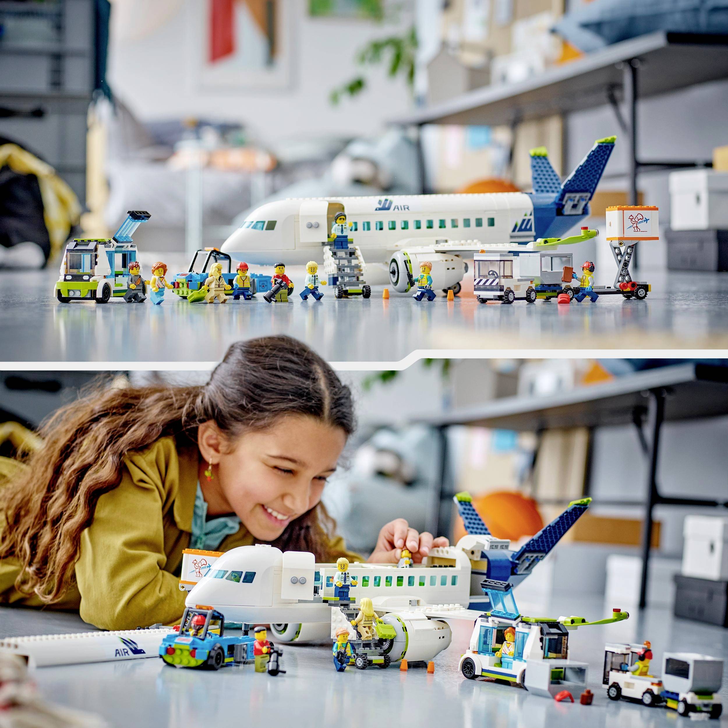 Ett leende barn leker på golvet med en detaljrik LEGO-flygplansuppsättning, inklusive passagerarfigurer och markfordon.