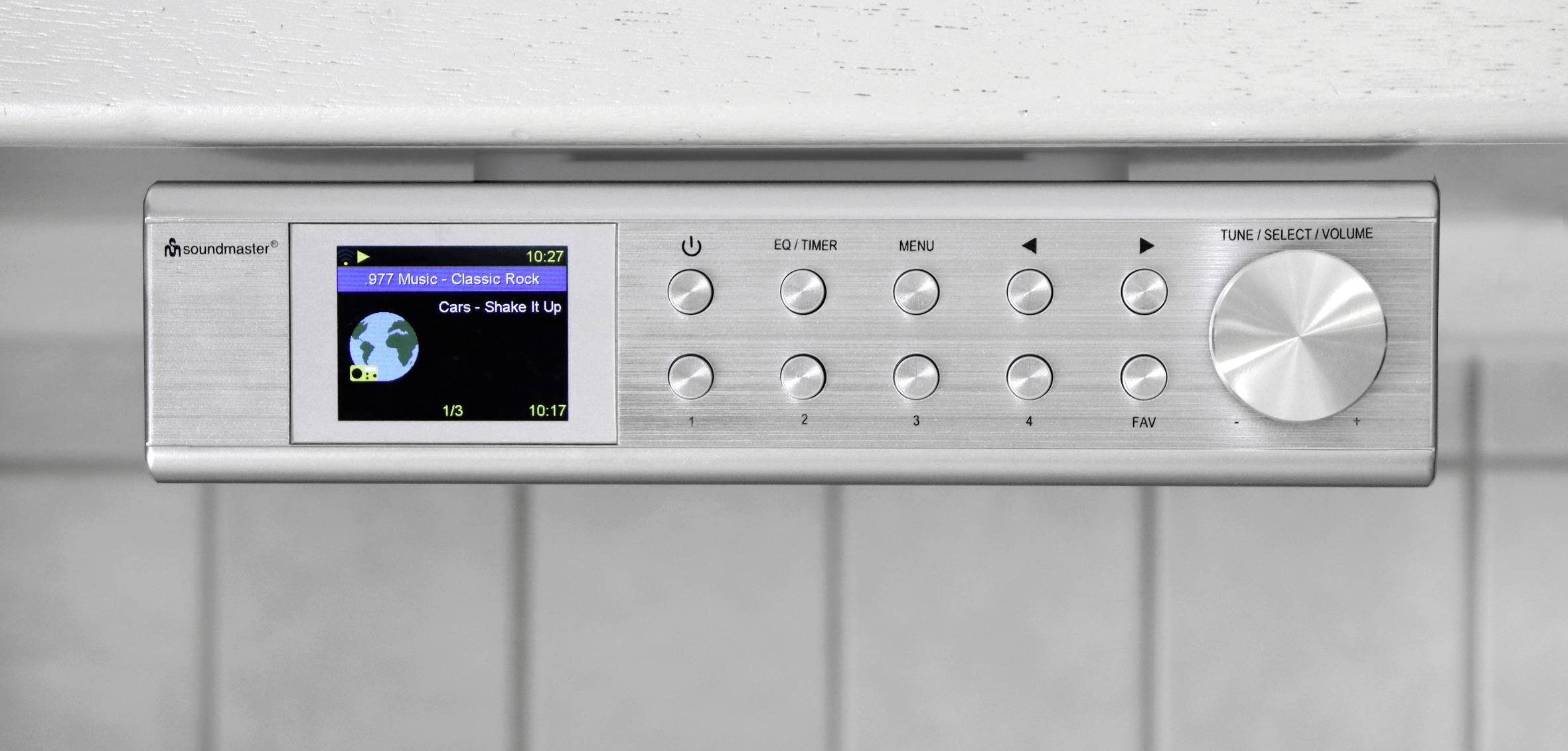 En silverfärgad köksradio med display som visar en radiokanal och låtinformation. Manöverorgan är placerade därunder.