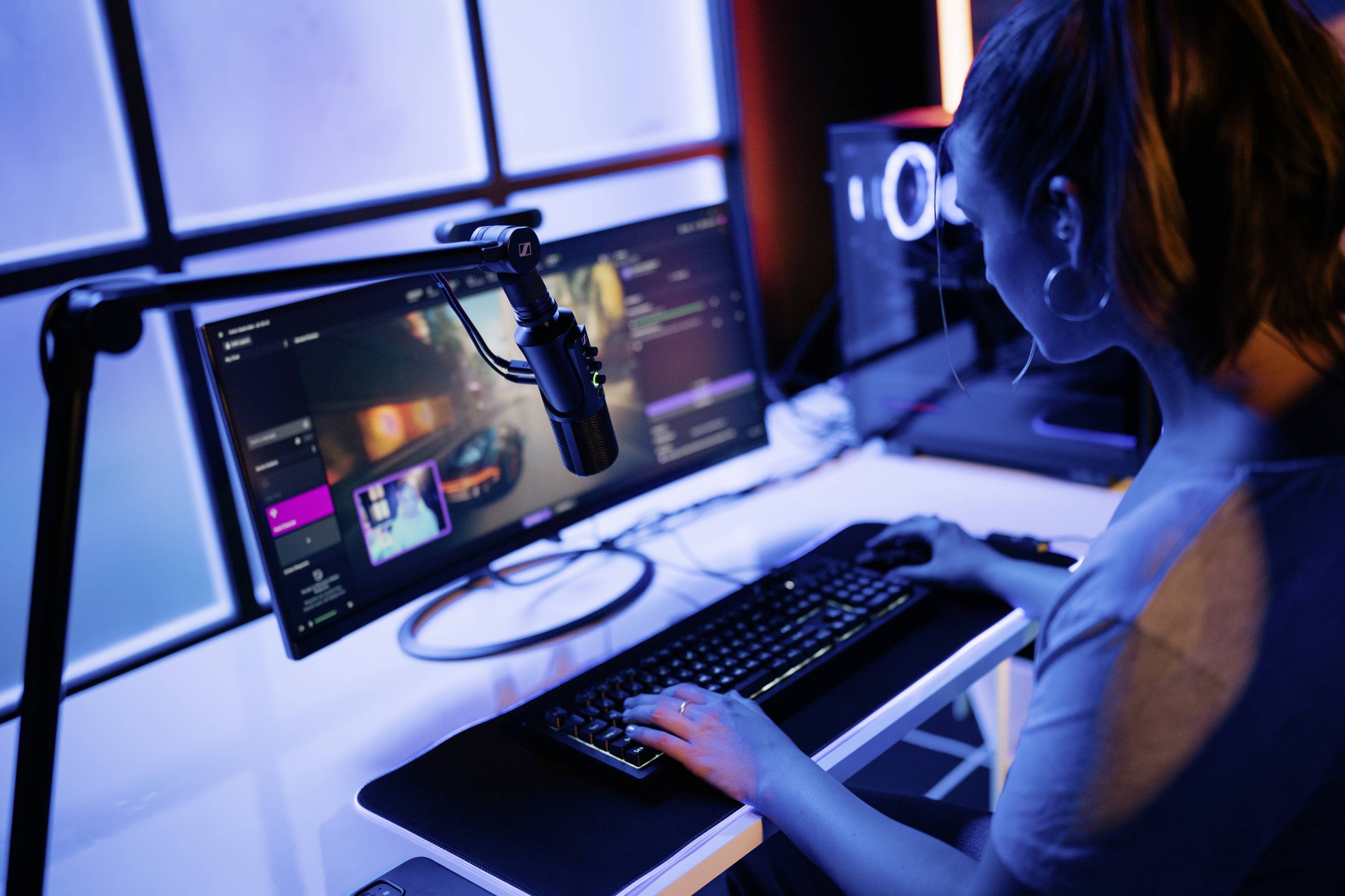 En person arbetar vid en dator med en stor skärm och ett mikrofon, troligen under streaming eller videoeditering.