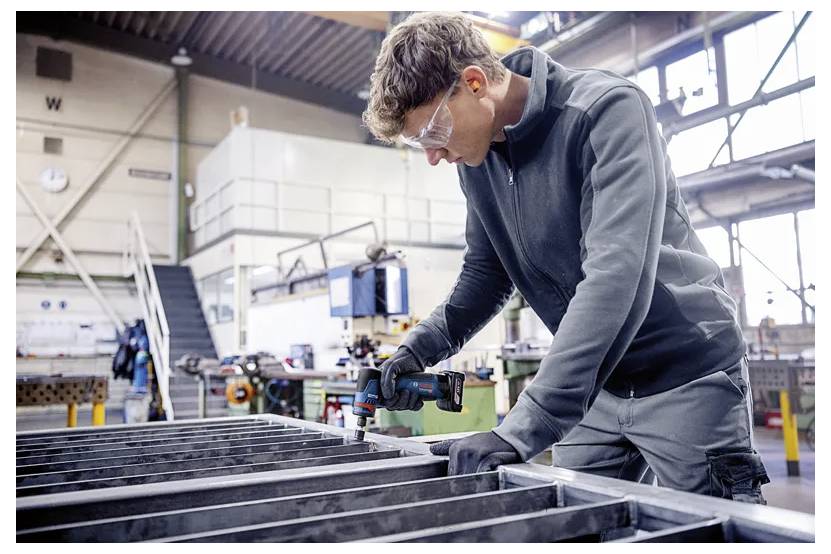 Arbetare i säkerhetglasögon och handskar som mäter eller monterar en metallram i en verkstad eller fabrik.
