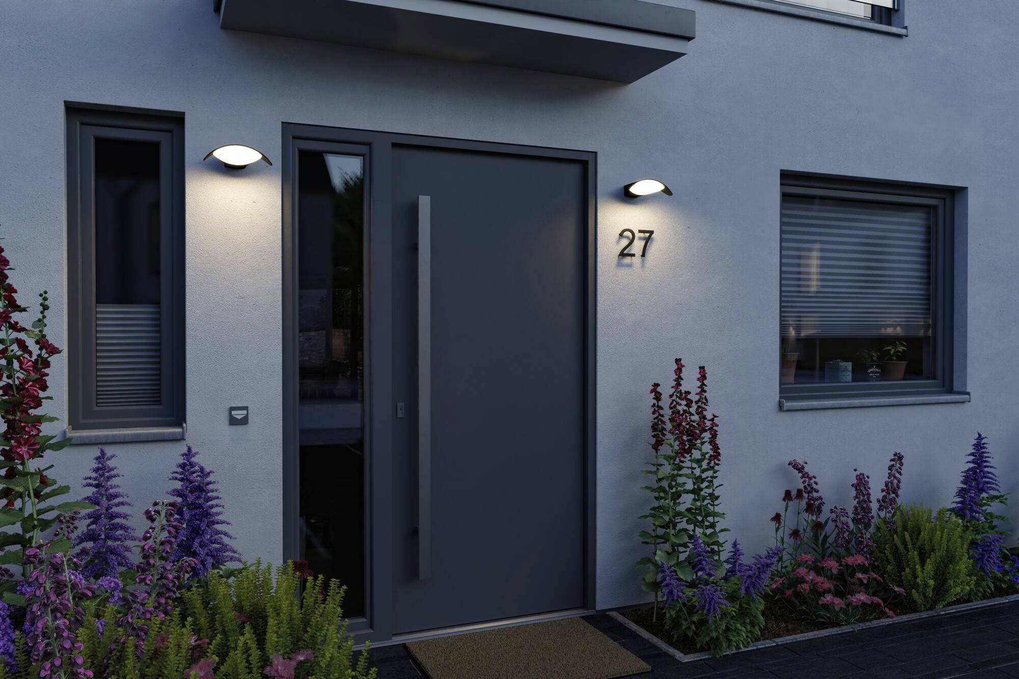 En modern ytterdörr till ett hus vid skymningen, omgiven av blommande blommor och belyst av två utomhusarmaturer. Husnummer '27'.