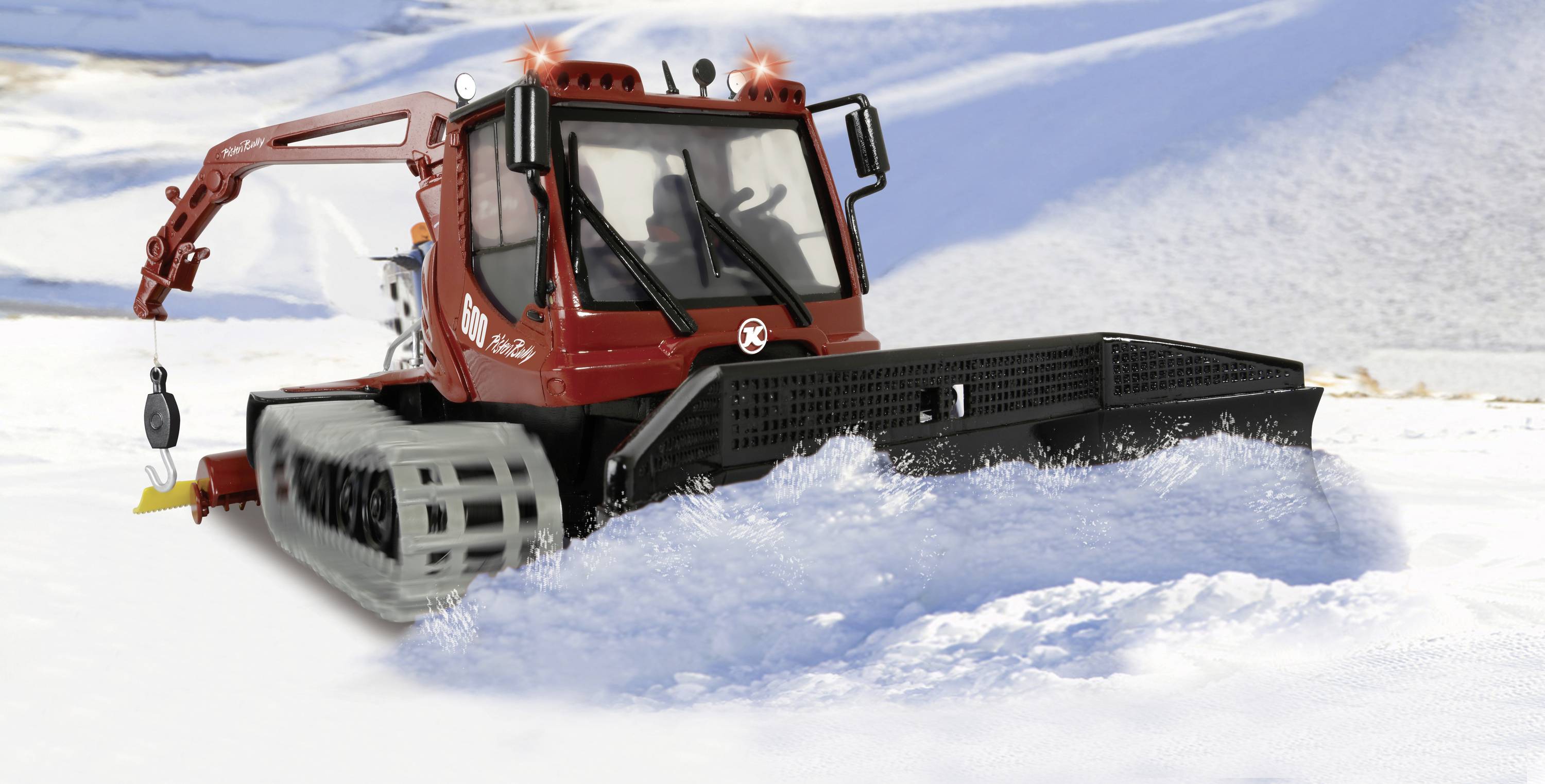 En röd pistmaskin jämnar ut snön på en skidpist i ett berglandskap. Himlen är blå och omgivningen är täckt av snö.