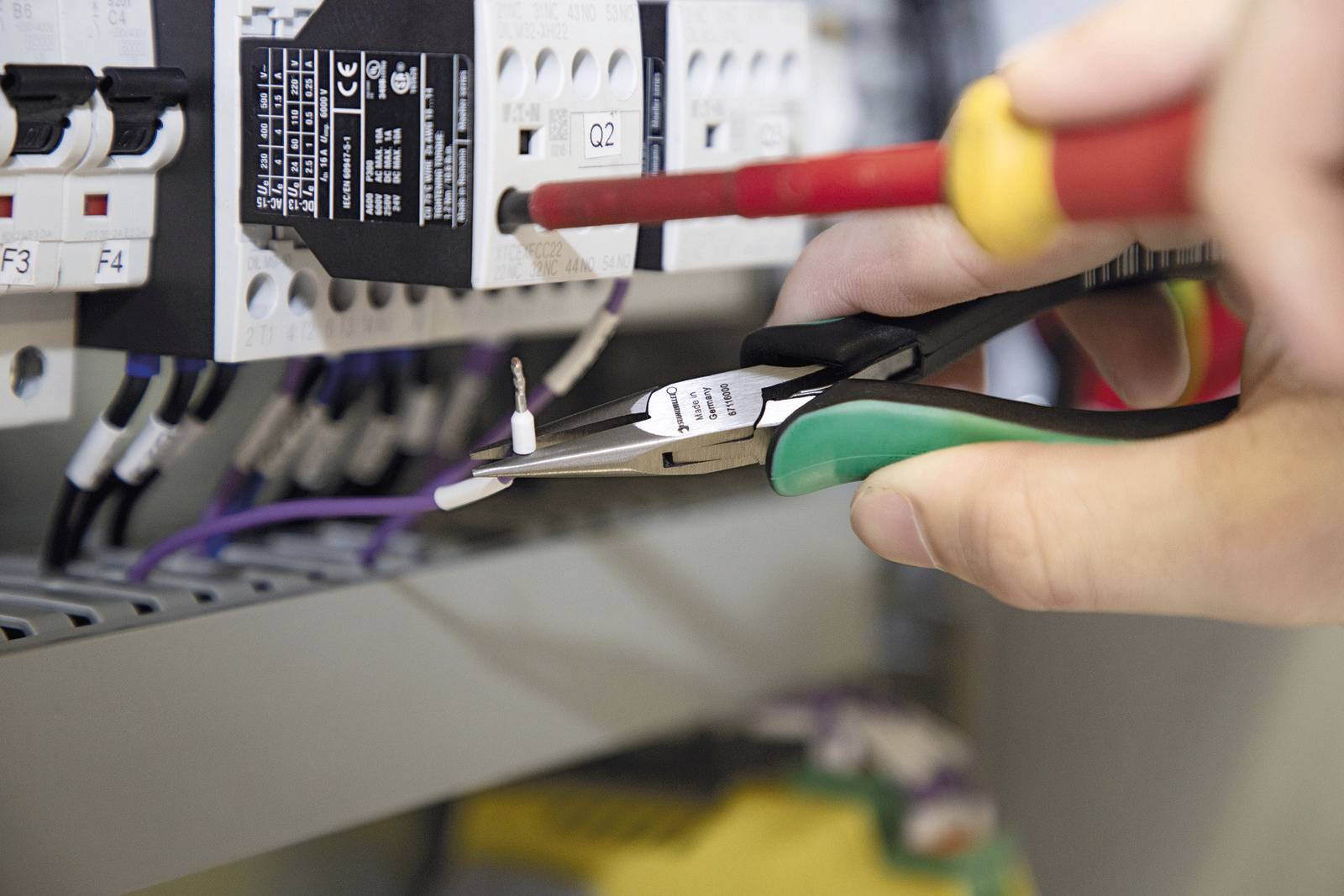 En person använder en skruvmejsel och en tång för att ansluta elektriska kablar i en elcentral.