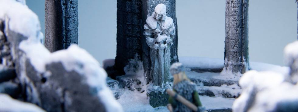 En snötäckt staty står framför gamla, förfallna pelare. En person närmar sig statyn genom snön. Vintrig atmosfär.