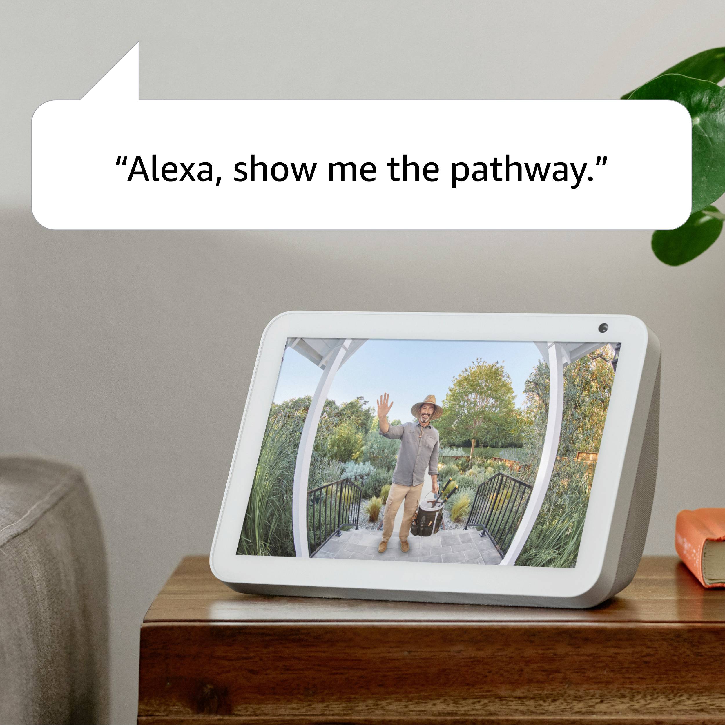 Smart-enhet på bordet visar ett foto av en leende man på en väg i en grön trädgård. Citat på enheten: 'Alexa, visa mig vägen.'