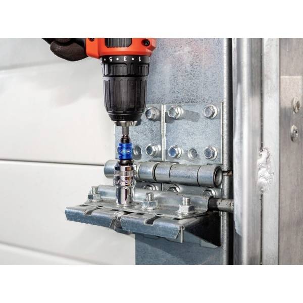 En person använder en borrmaskin för att installera eller ta bort en bult på ett gångjärn av metall, och visar en närbild av verktyget och hårdvaran.