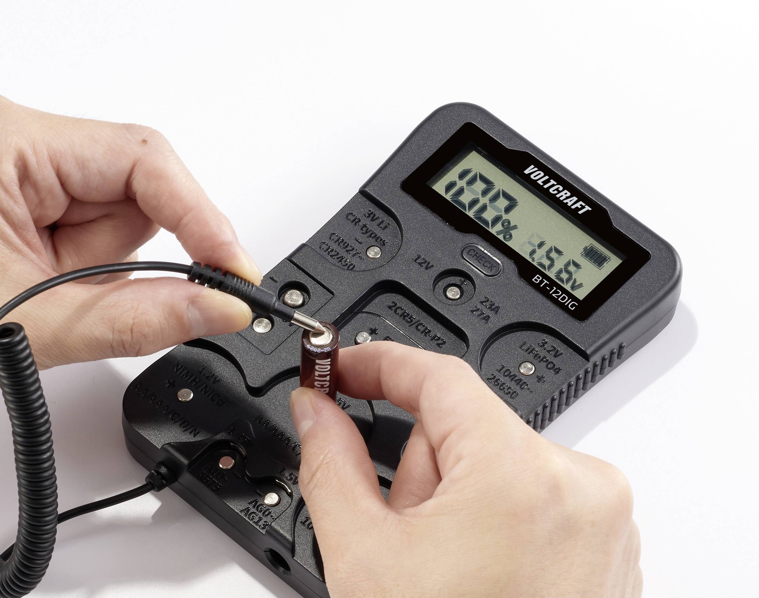En person mäter kapaciteten hos en kondensator med ett digitalt multimeter. Displayen visar '102,0%'.