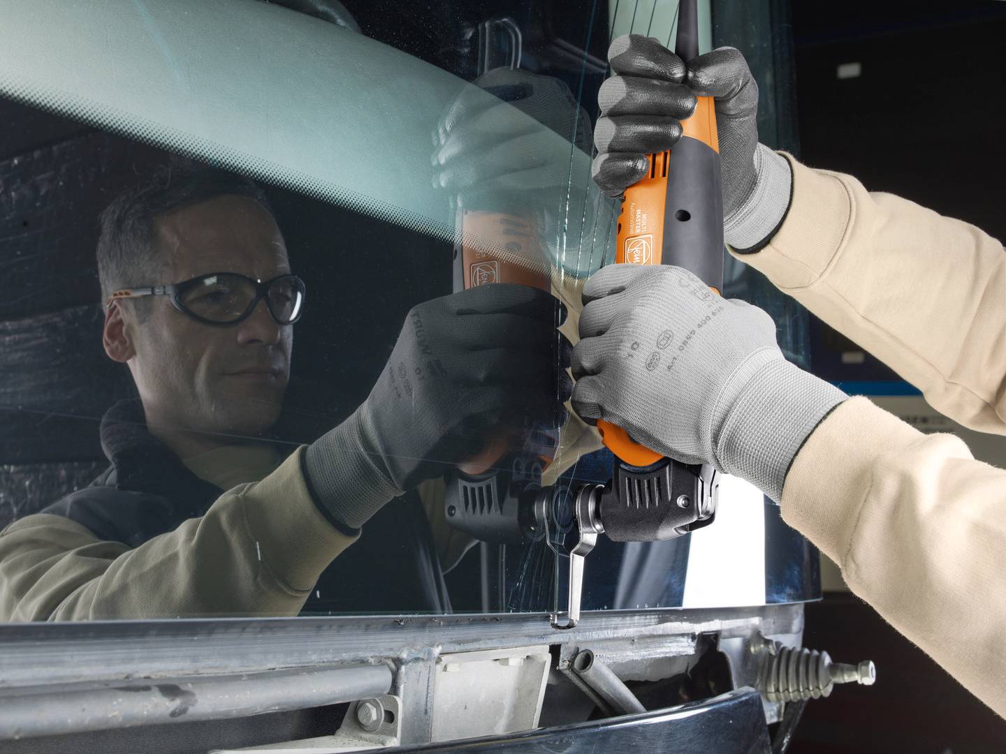 En person med skyddsglasögon och handskar använder ett elektriskt verktyg för att reparera eller byta ut en bilruta.