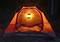 Ett orangefärgat tält står i mörkret, upplyst inifrån av en ljus lykta som lyser upp ingången.