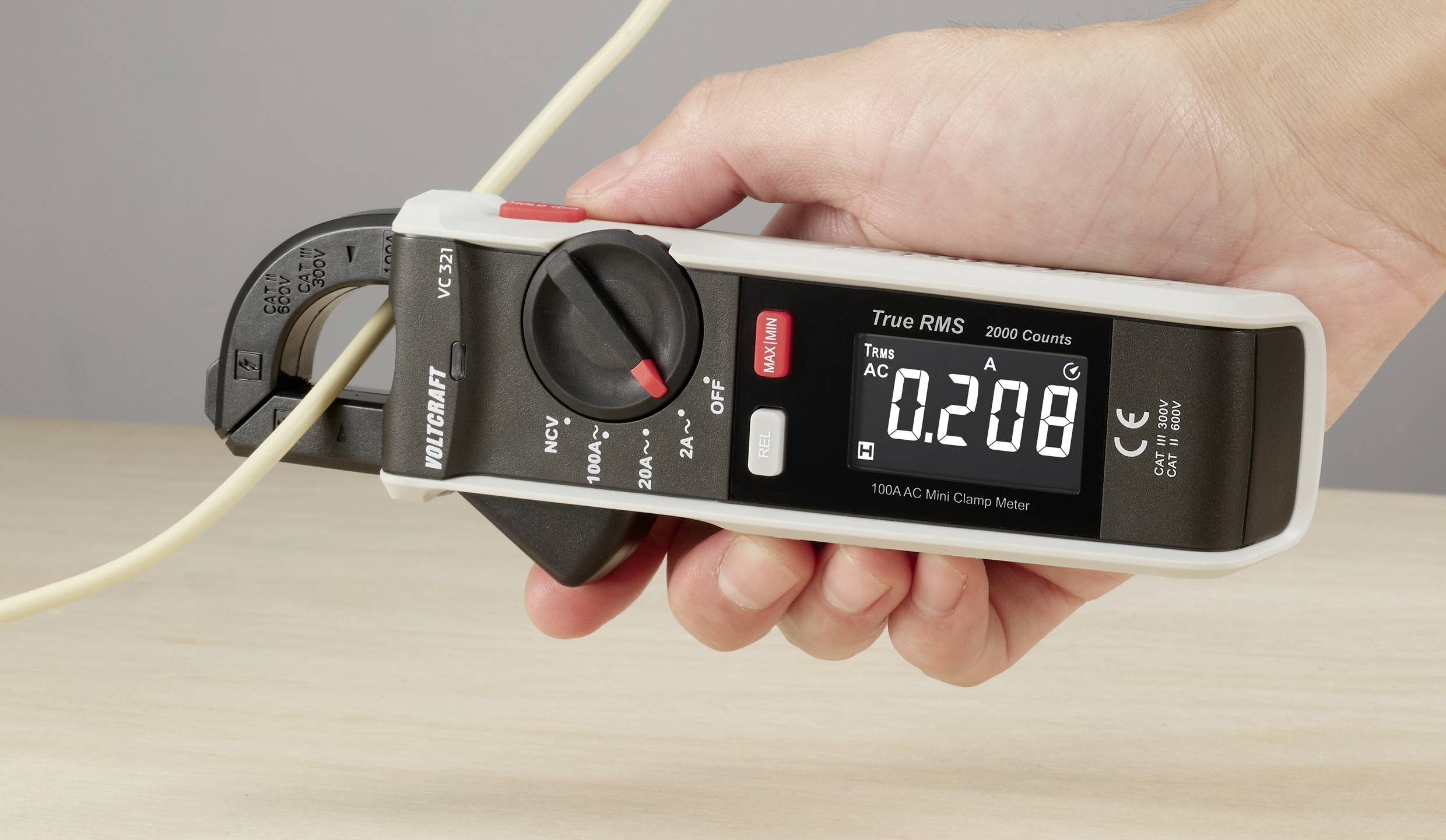 En hand håller ett digitalt strömtångemultimeter vid en kabel som visar ett värde på 0,208 ampere på displayen.