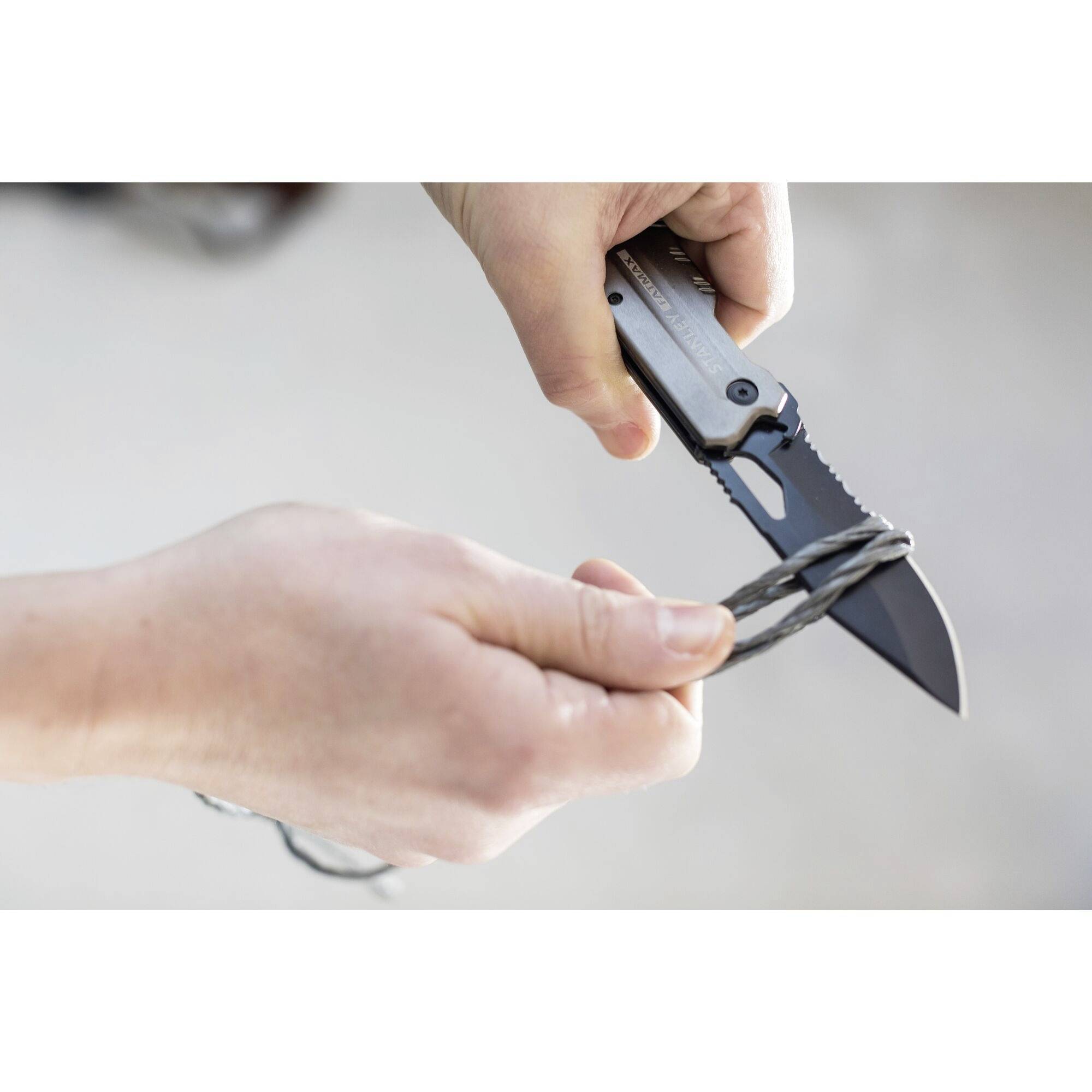 En hand håller en kniv medan den andra handen håller ett metallföremål eller en tråd nära bladet.