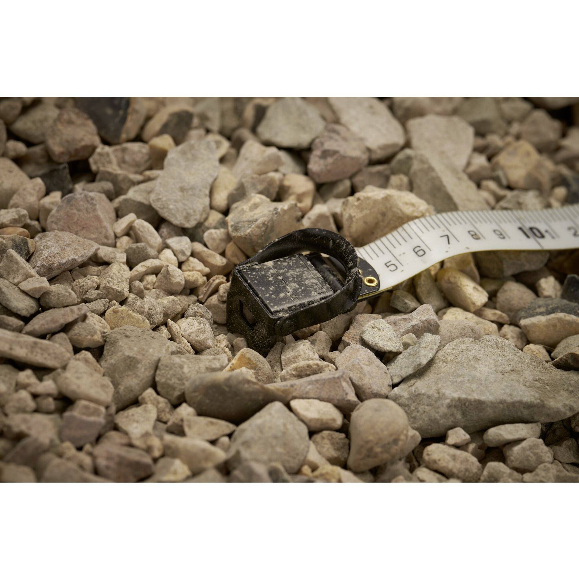 Ett måttband ligger på en grusbotten, omgivet av små stenar. Måttbandet visar ungefär 10 centimeter.