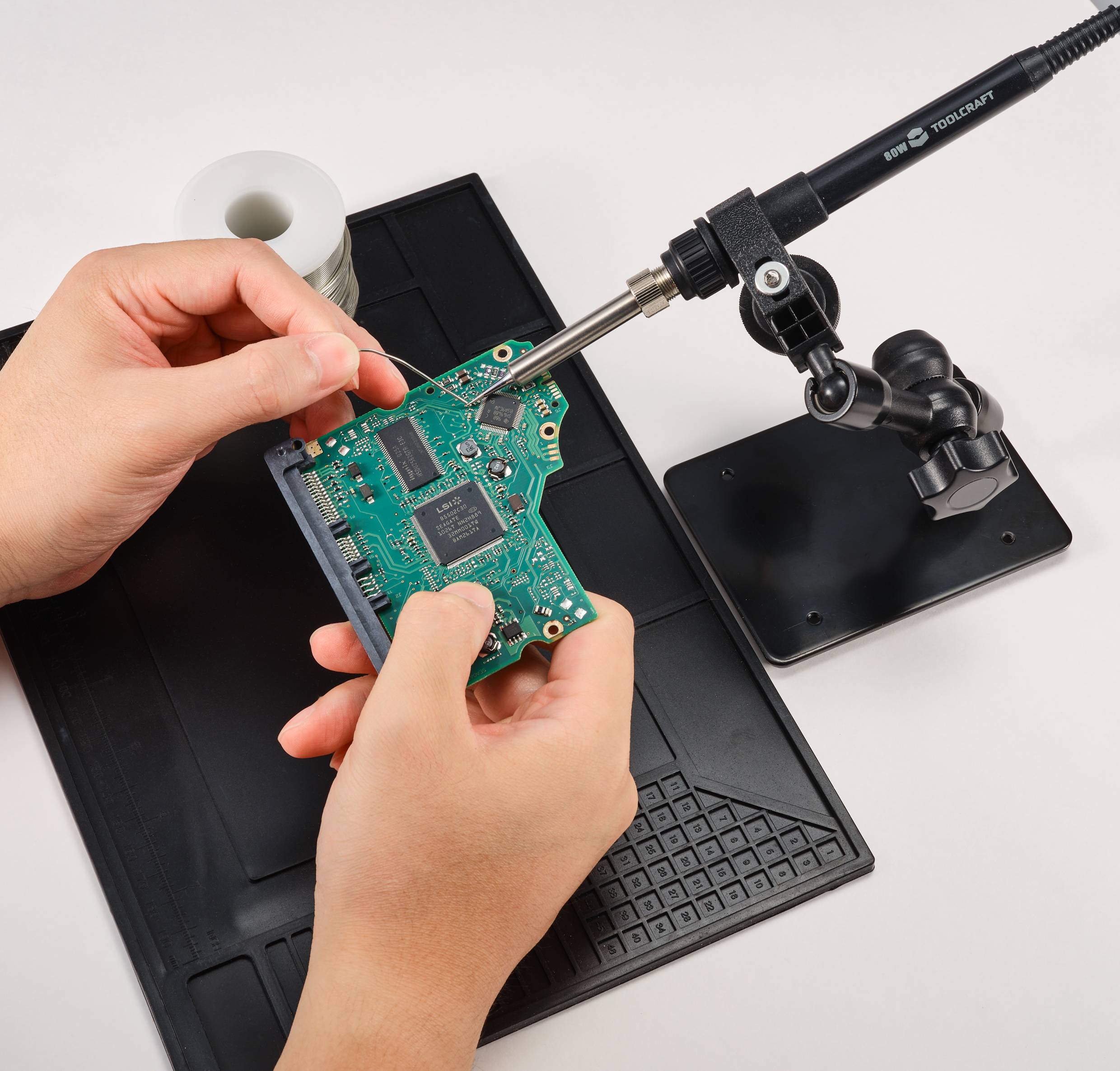 En person löder ett grönt kretskort med en lödkolv. Scenen visar precisionsarbete vid elektronikreparation.