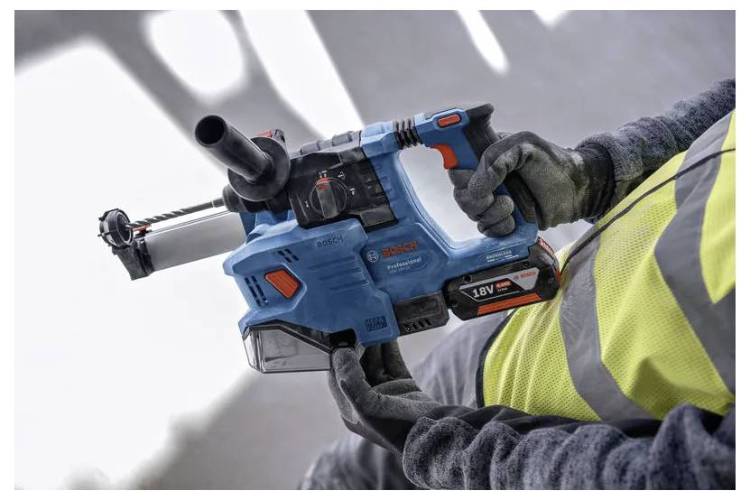 En person som bär en gul varselväst håller en blå sladdlös Bosch rotationshammarborrmaskin märkt '18V SYSTEM.'