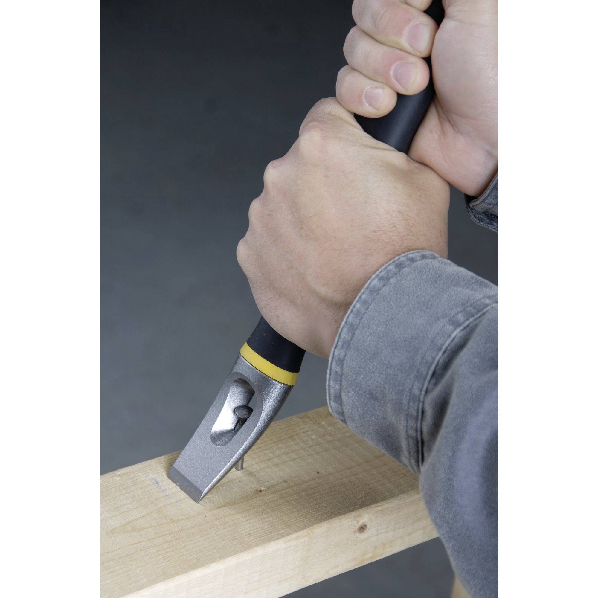 En person håller i en hammare med båda händerna. Hammarens huvud träffar en spik i ett träbräde.