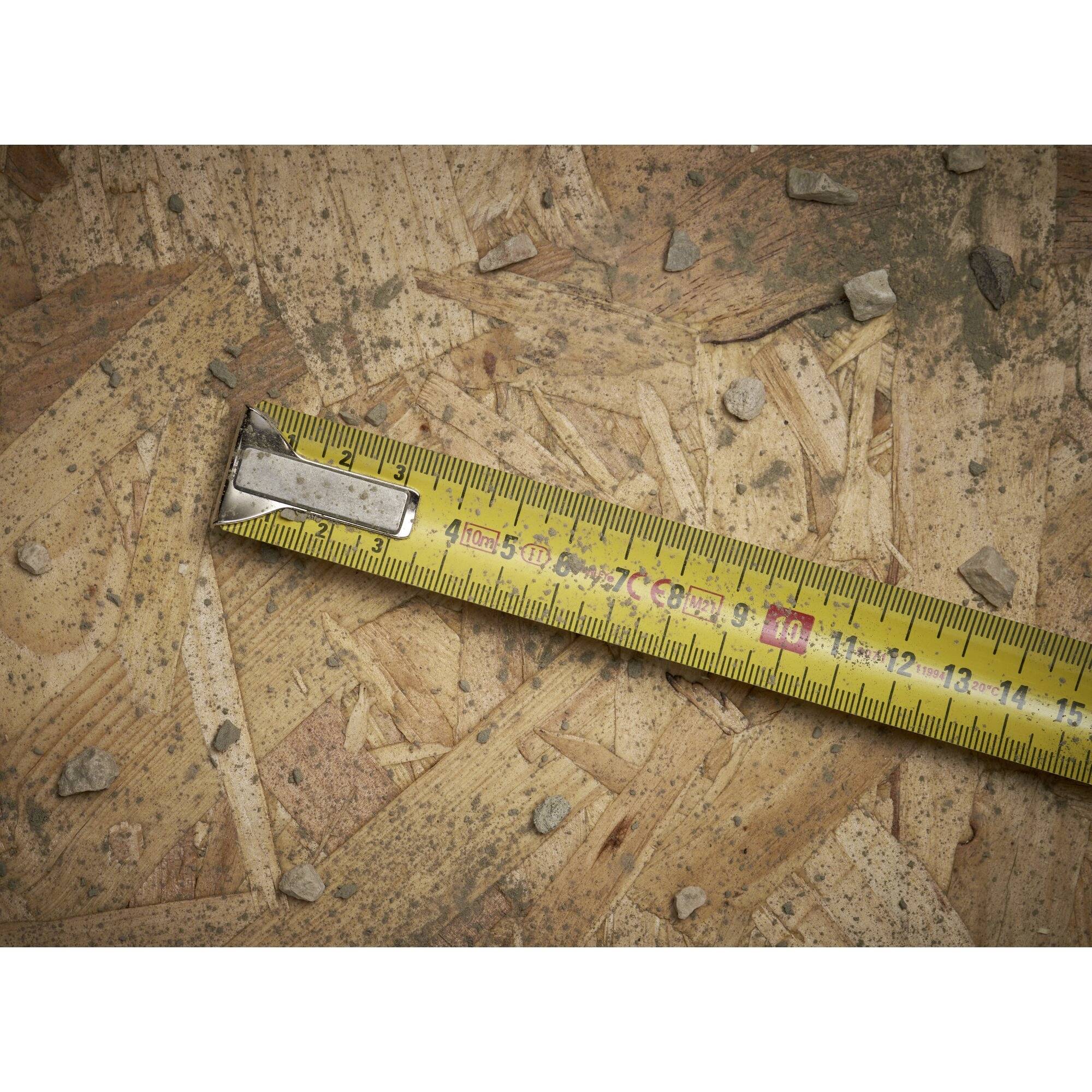 Ett måttband ligger snett på en träyta, omgivet av små stenar.