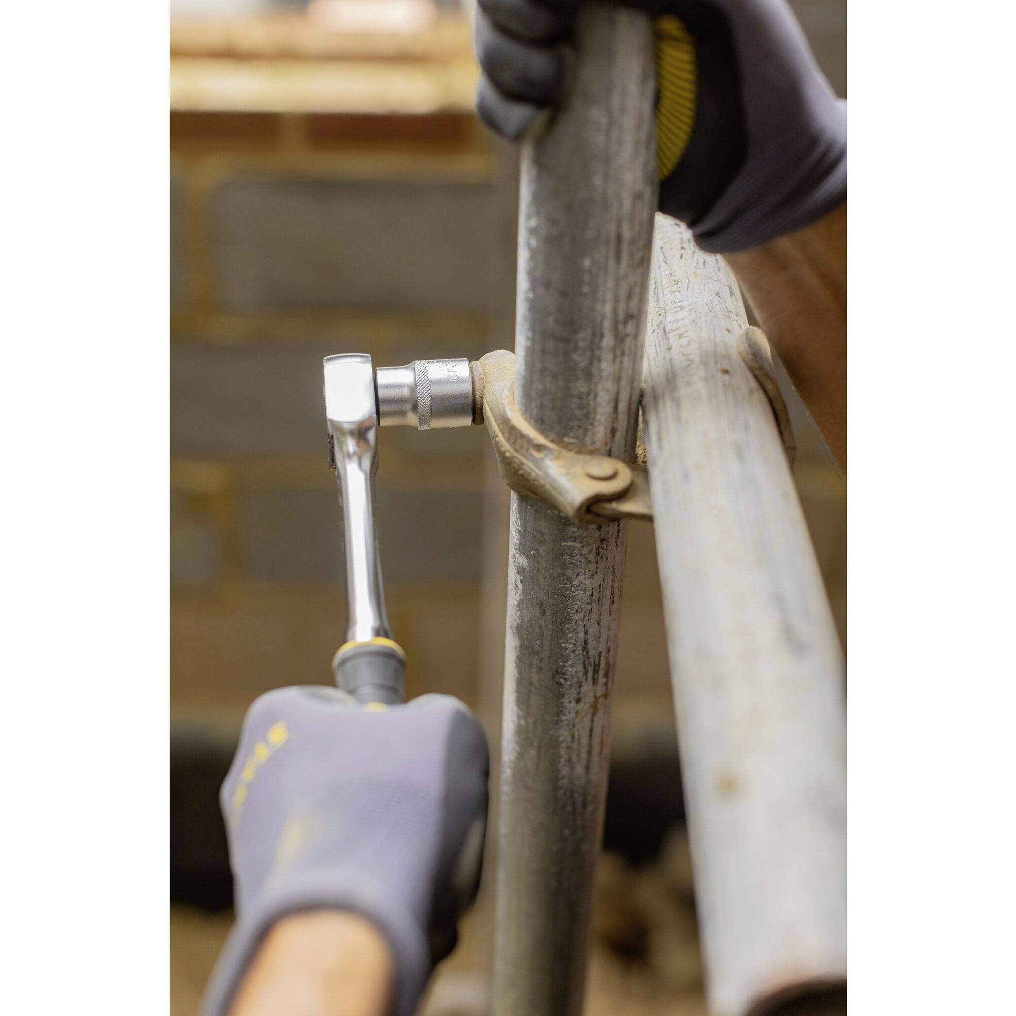 En person med handskar reparerar ett metallrör med en justerbar skiftnyckel och en hammare; fokus på verktyg.