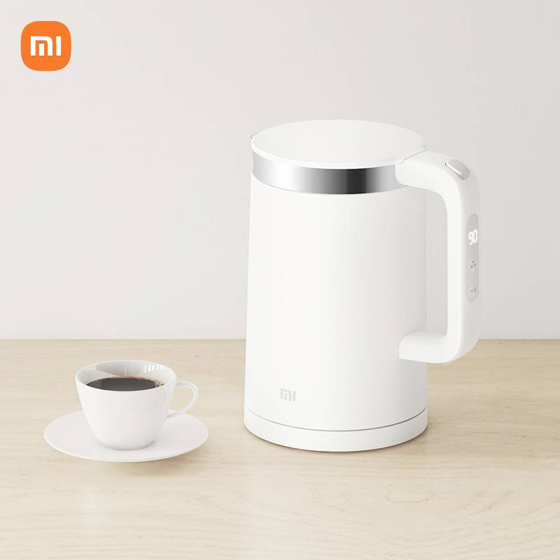En vit elektrisk vattenkokare står på ett bord bredvid en kopp kaffe. Xiaomi-logotypen finns i övre vänstra hörnet.