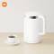En vit elektrisk vattenkokare står på ett bord bredvid en kopp kaffe. Xiaomi-logotypen finns i övre vänstra hörnet.