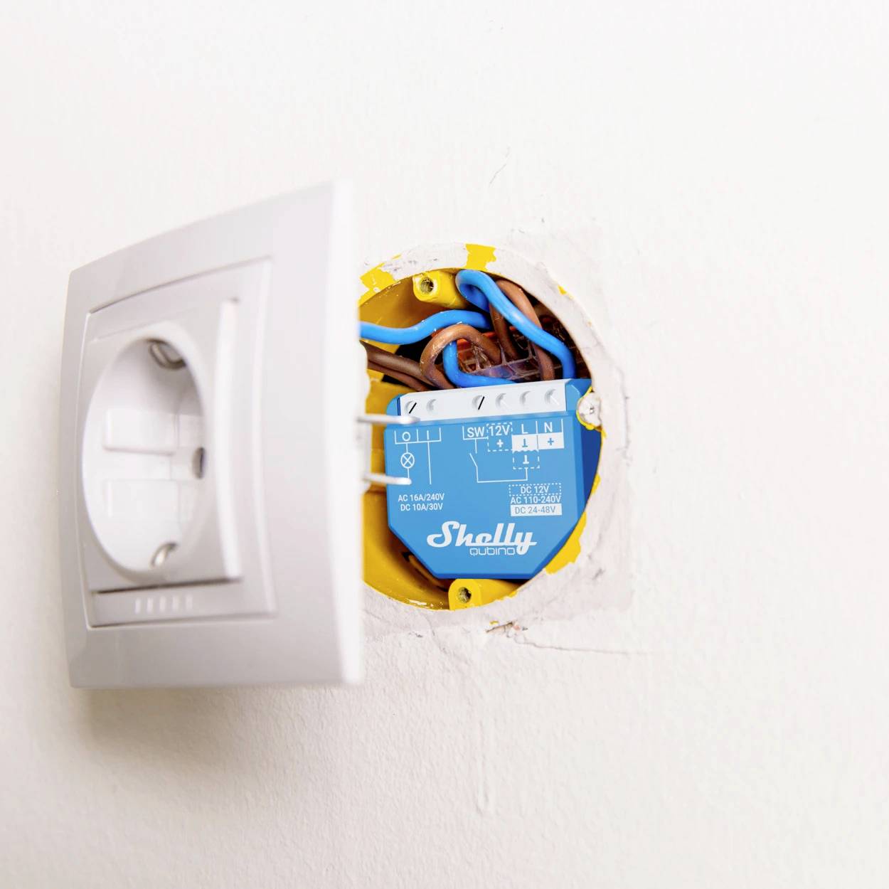 En öppnad vägguttag visar kabeldragningen och en integrerad blå Shelly-switch.