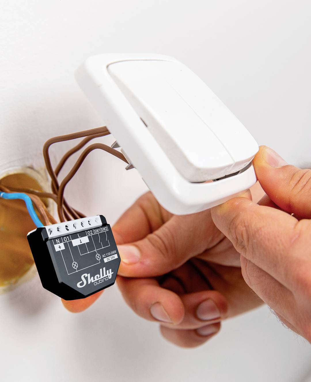 En person installerar en Shelly-switch på en vägg, varvid flera kablar ansluts.