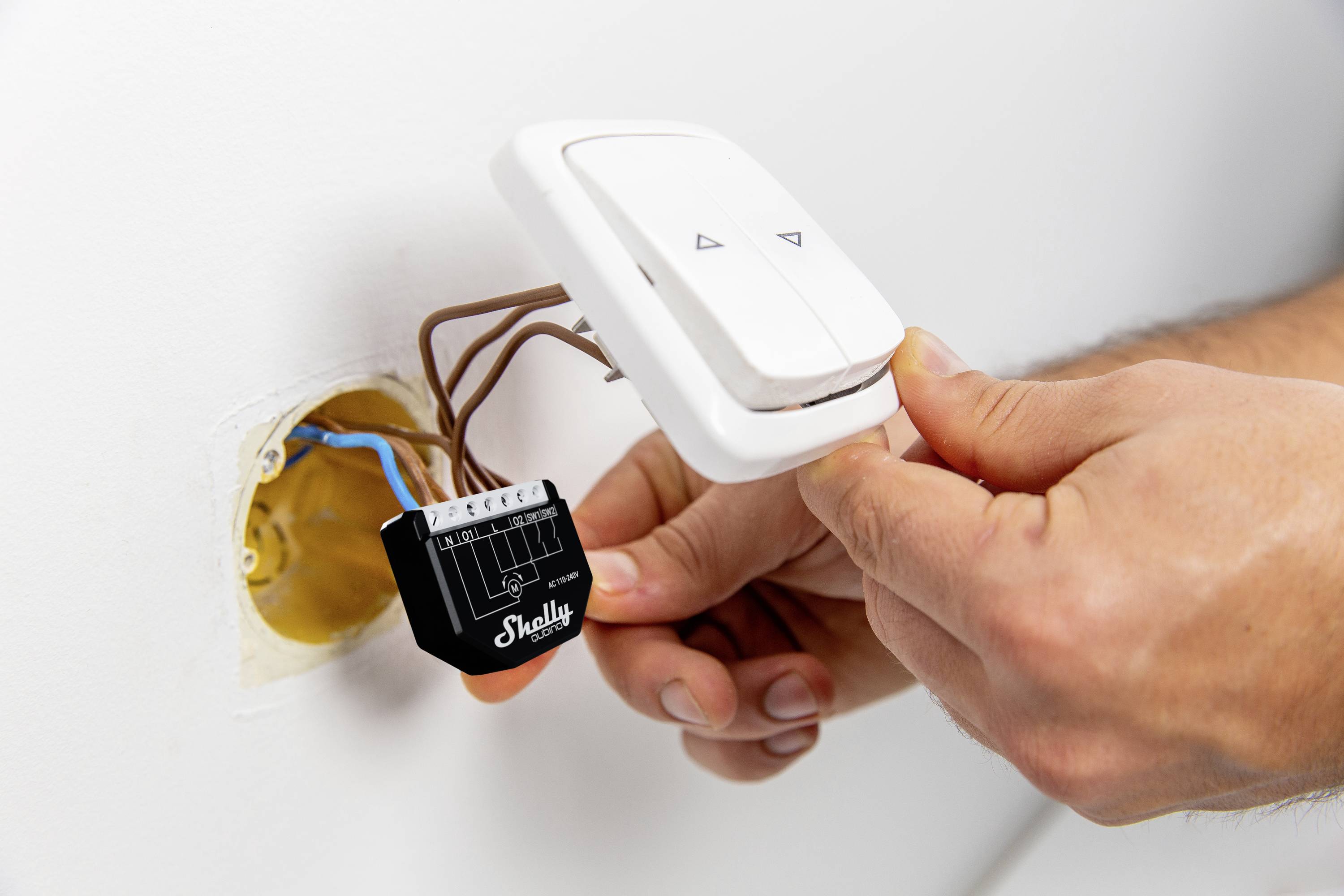 Handen monterar en smart switch med ett Shelly-modul i ett vägguttag. Kabeldragningen är synlig.
