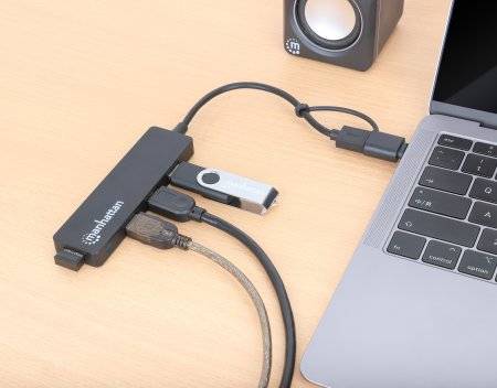Multianslutningsenhet förbinder bärbar dator via USB-C med USB-minne, HDMI-kabel och strömadapter. Högtalare i bakgrunden.