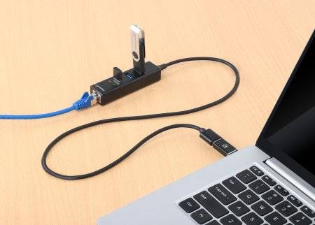 Bärbar dator ansluten till en USB-hubb som är värd för ett USB-minne och en blå Ethernet-kabel, på ett träbord.