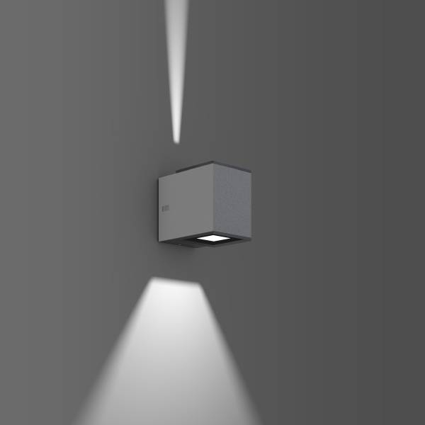 En modern vägglampa projicerar ljus uppåt och nedåt på en grå vägg, vilket skapar en stilfull atmosfär.
