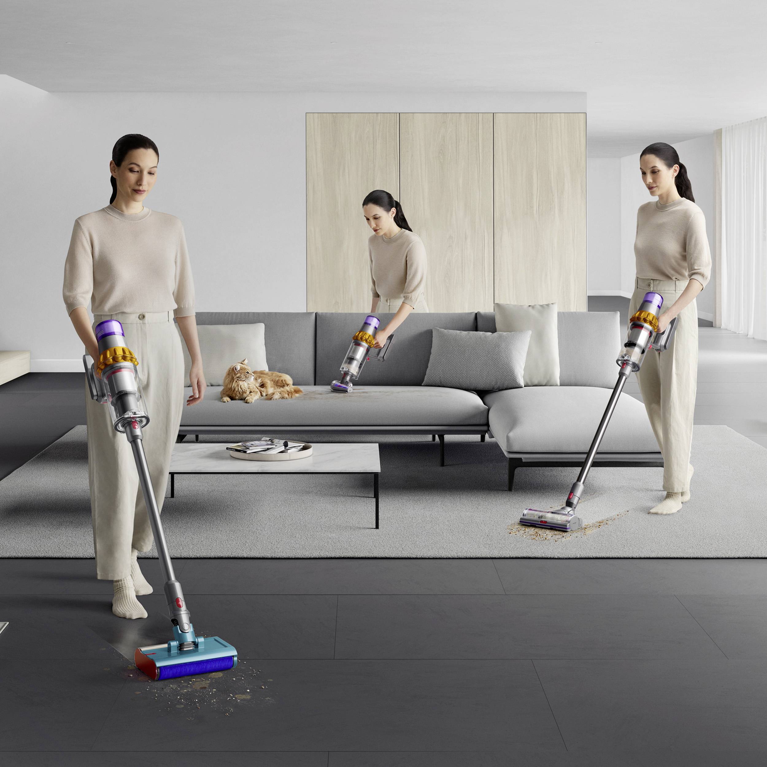 Tre personer dammsuger synkroniserat ett modernt, minimalistiskt inrett rum med en grå soffa och ett soffbord.