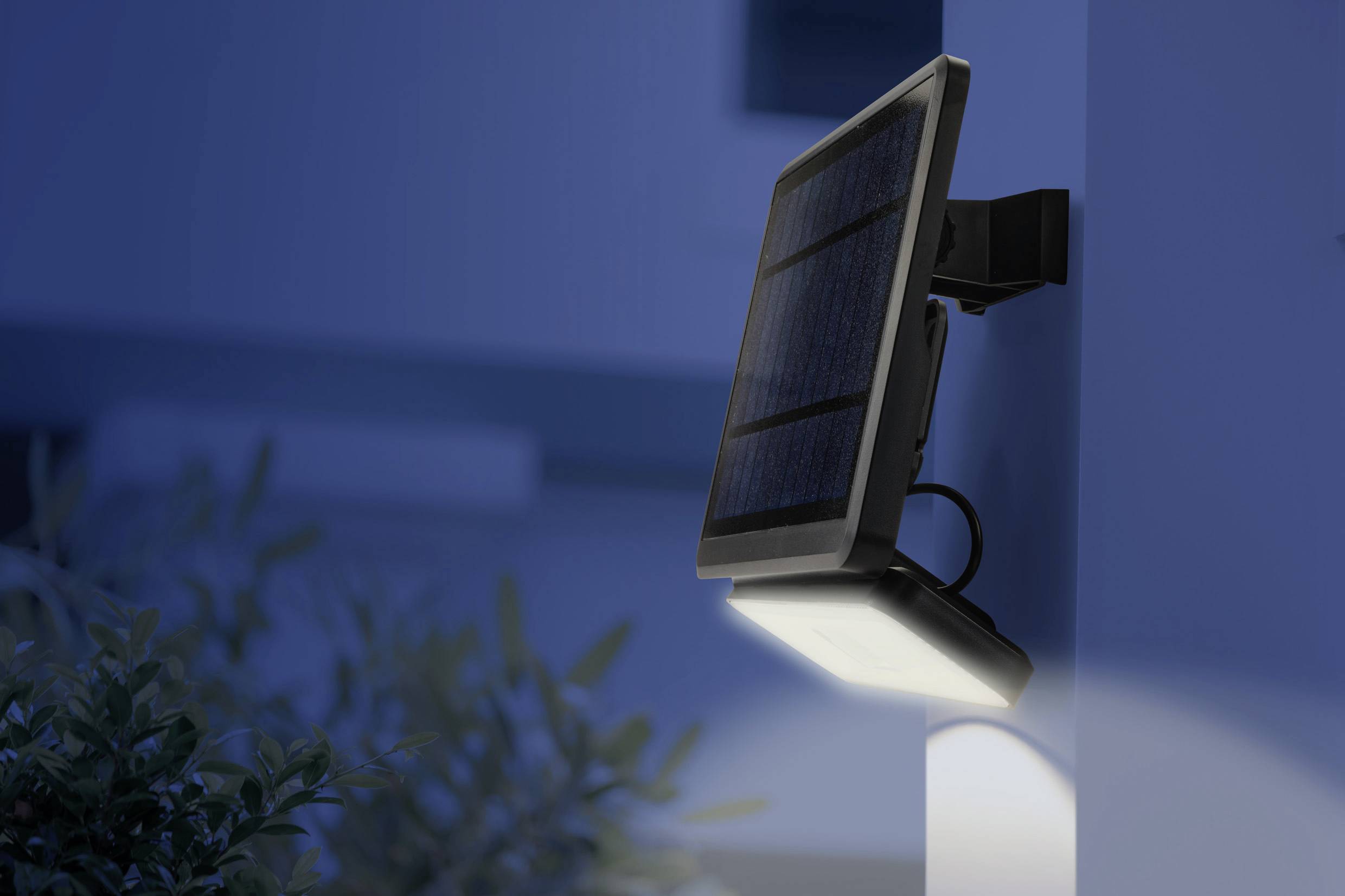 Sollampa på en vägg, lyser upp ett trädgårdsområde under natten. Modern och energieffektiv utomhusbelysning.