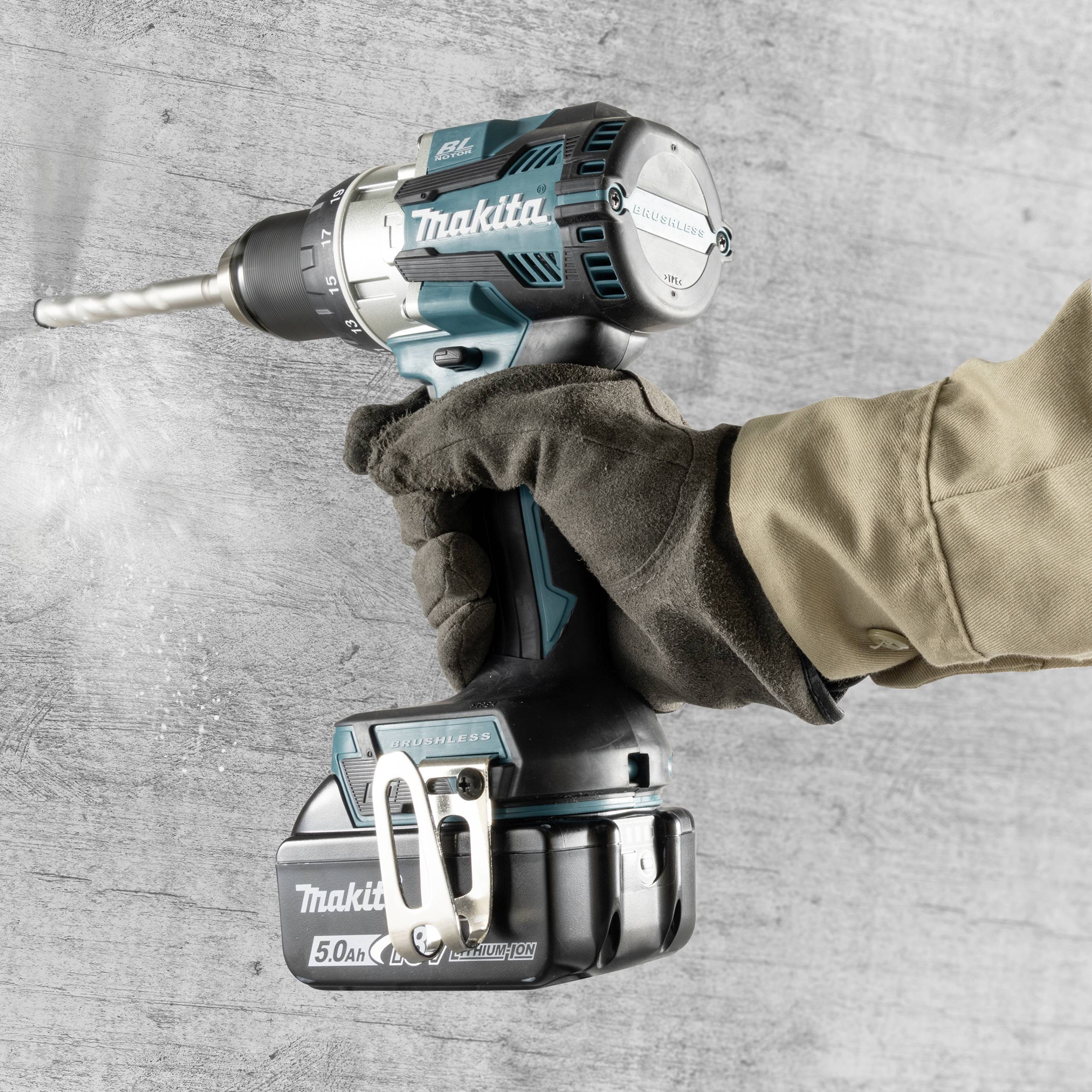 En arbetare borrar i en betongvägg med en sladdlös Makita-borrmaskin. Till vänster roterar borrmaskinens chuck och ett stabilt borrhuvud.