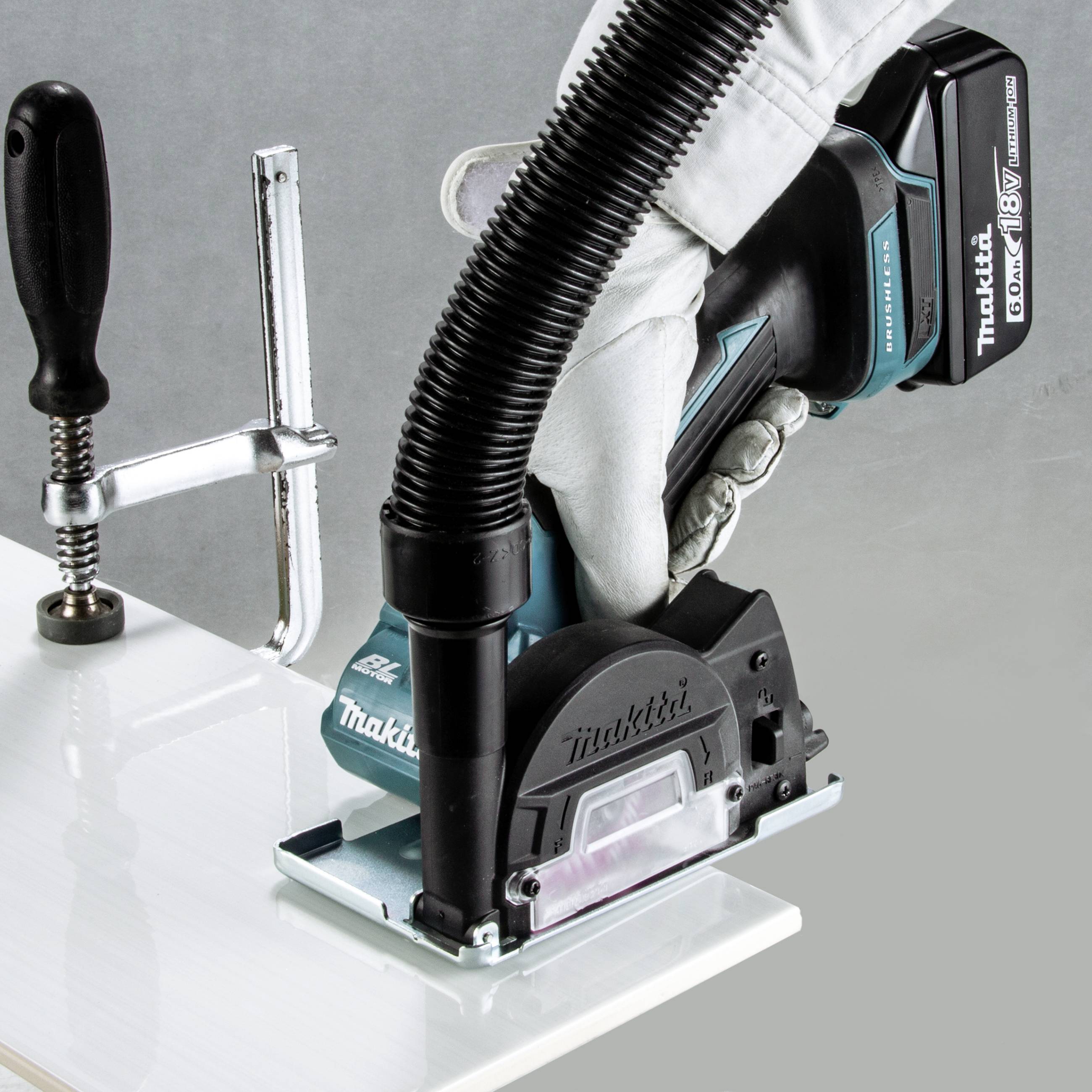 En hand håller ett Makita-elverktyg för att slipa ett metallstycke som är fastsatt i en arbetsbänk.