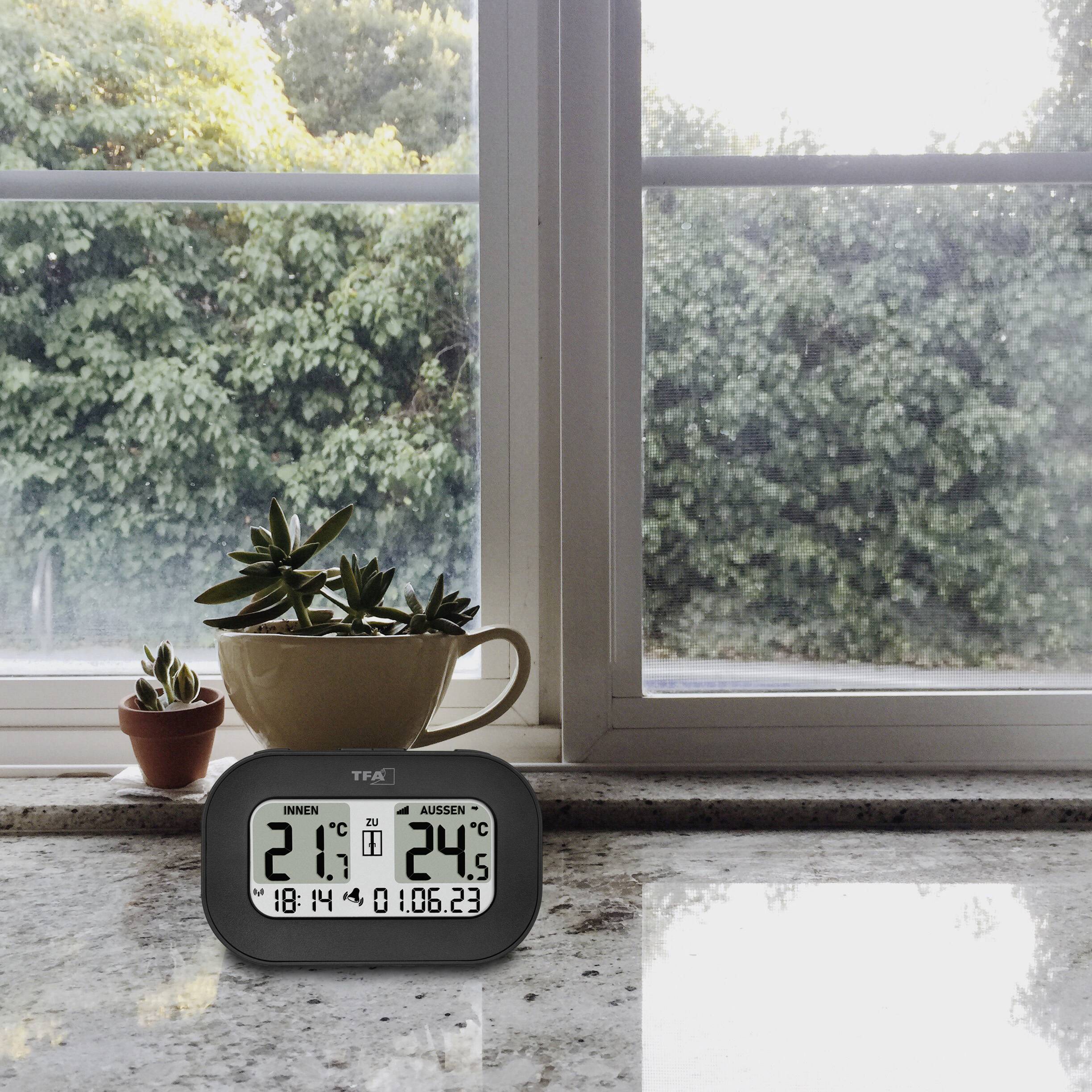 Termometer på fönsterbrädan visar 21,7°C inomhus, 20,6°C utomhus. Bakgrund: Fönster med växter, utsikt mot en grön trädgård.