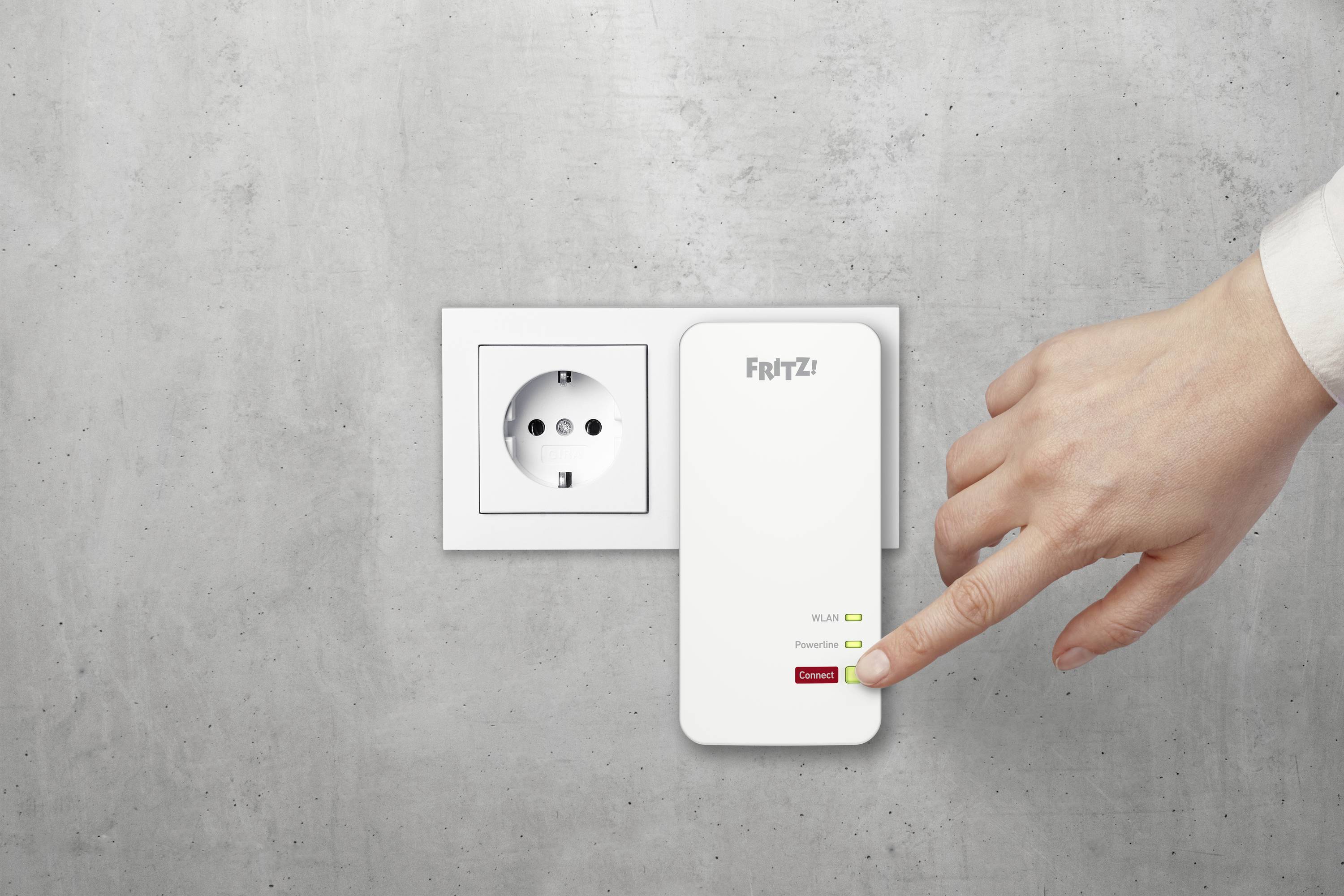 Någon sätter i en vit WiFi-repeater i ett vägguttag och trycker på den gröna 'Connect'-knappen för nätverksanslutning.