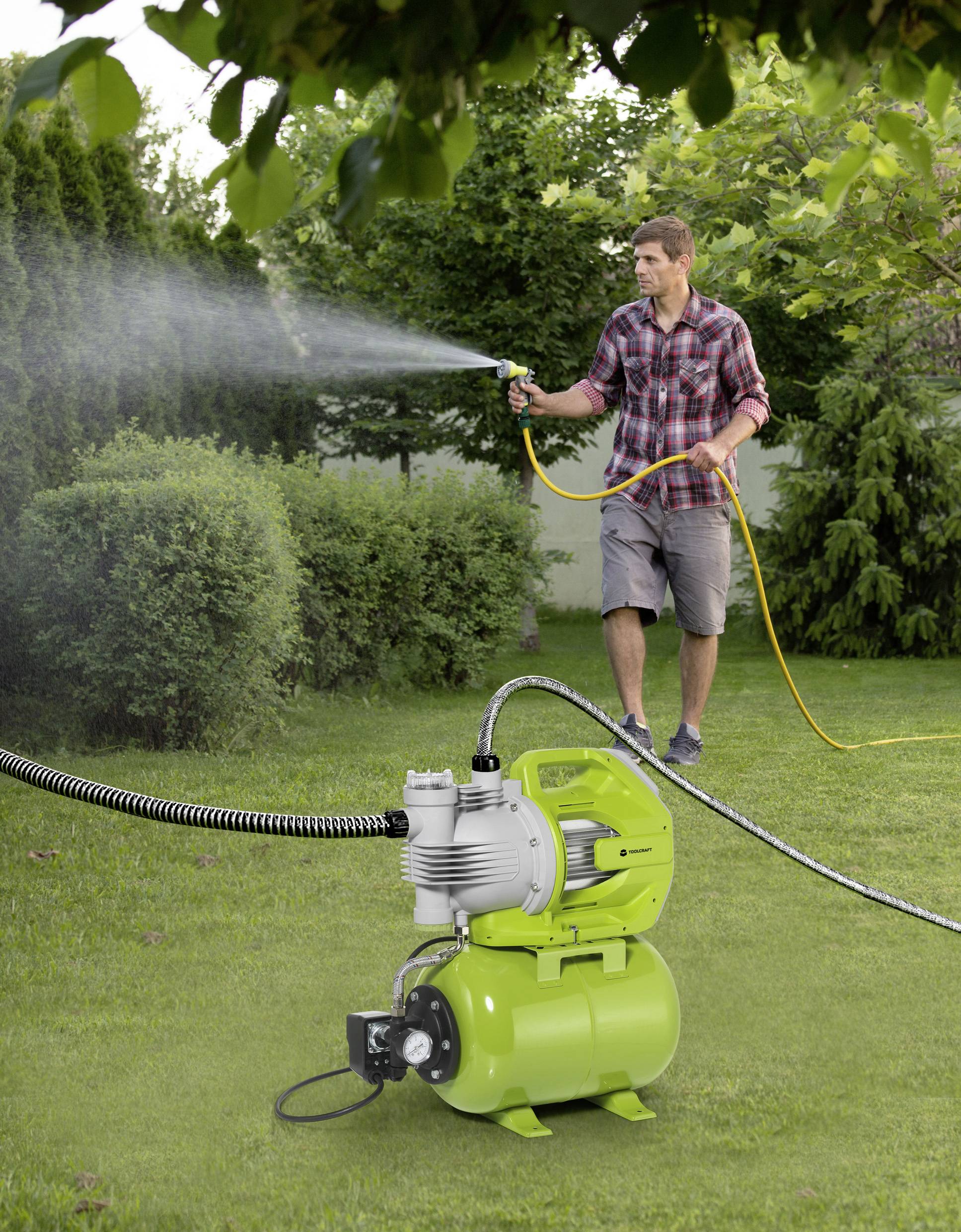 En man vattnar en gräsmatta med en vattenslang, medan en grön vattenpump syns i förgrunden.