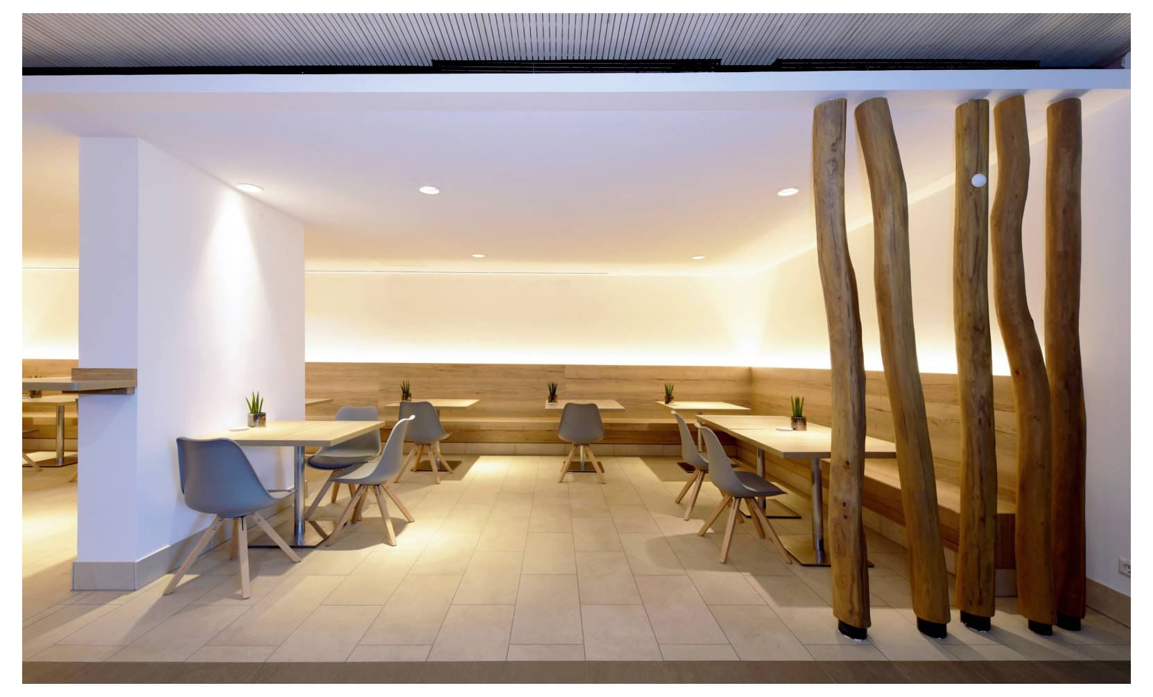Modern minimalistisk restauranginteriör med trämöbler, varm ambientbelysning och dekorativa träpelare nära entrén.