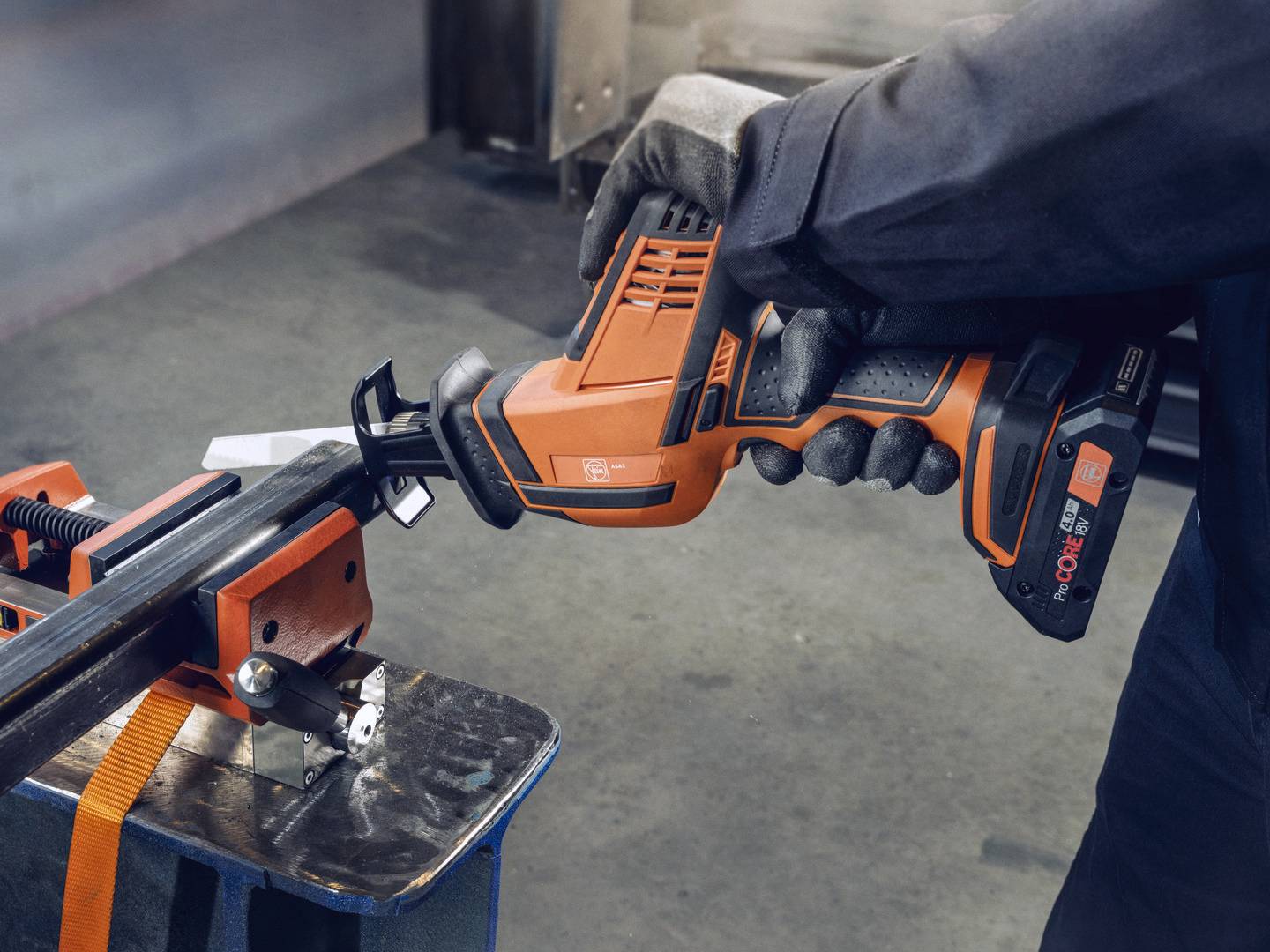 En person sågar ett metallrör med en elektrisk handsåg, som är fastklämt i ett skruvstäd.