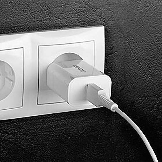 En laddare är isatt i ett vägguttag. En kabel är ansluten till laddaren och leder ut till höger utanför bilden.
