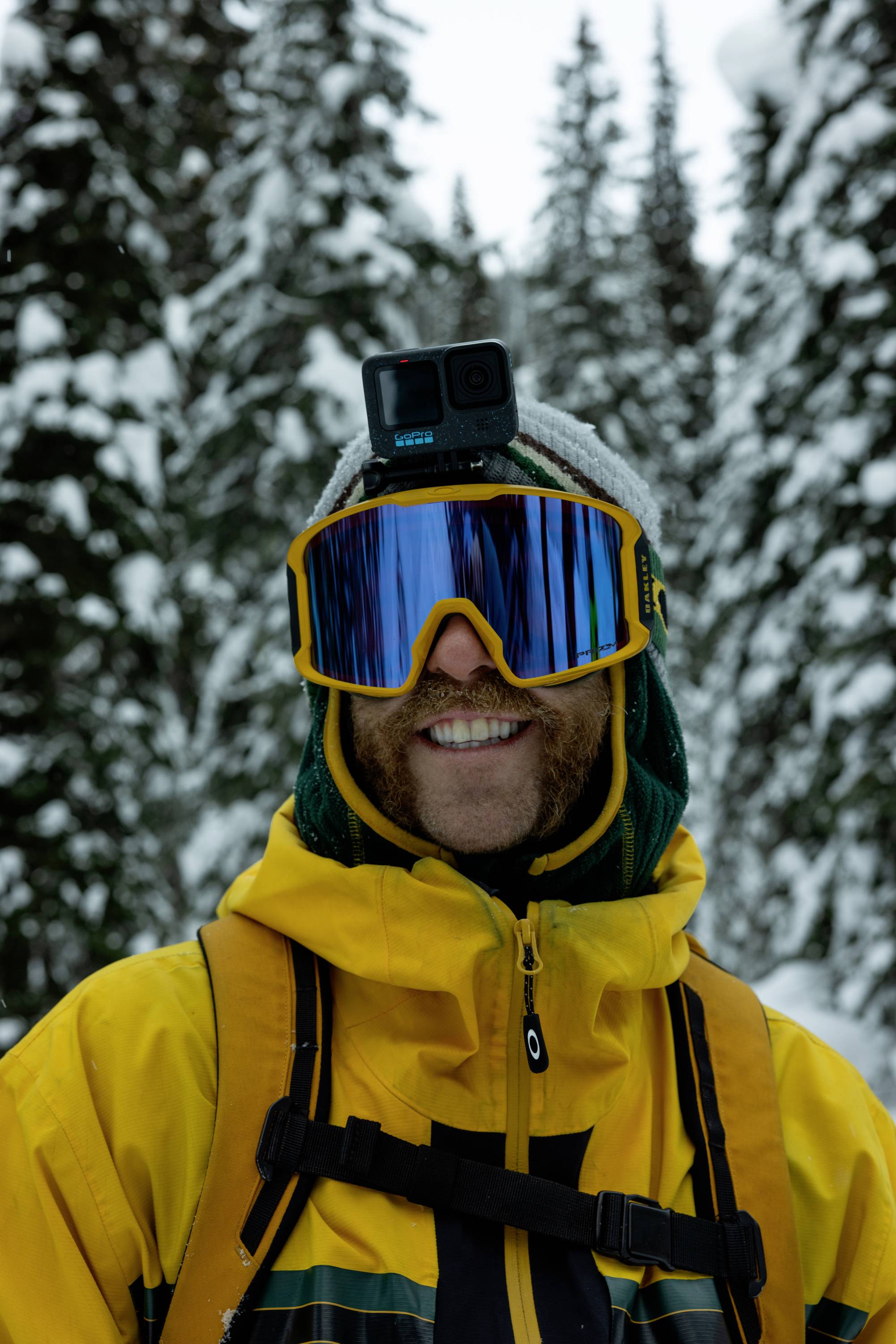 En person i gul-svart skidmundering står i en snötäckt skog. De bär glasögon och har ett kamera monterat på hjälmen.