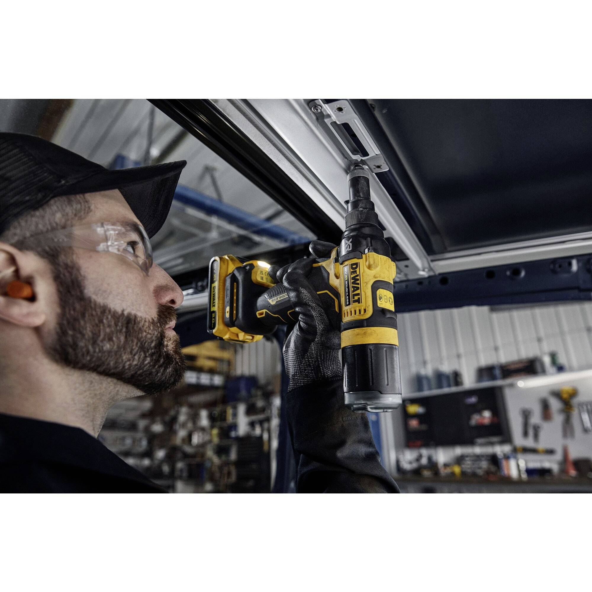 En arbetare i skyddsutrustning använder en skruvmejsel för att fästa en metallstruktur i en verkstad.