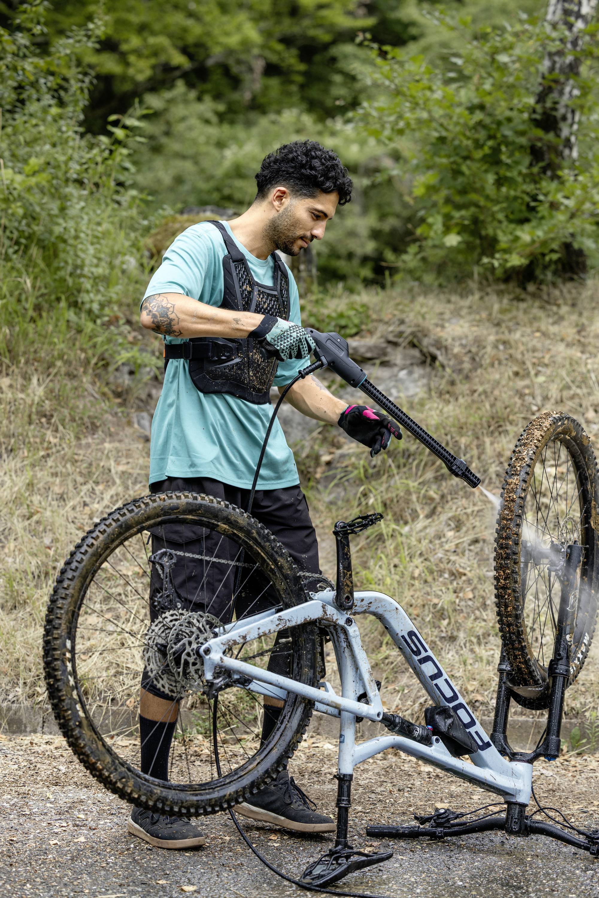 En man rengör en mountainbike med en högtryckstvätt på en väg i skogen.